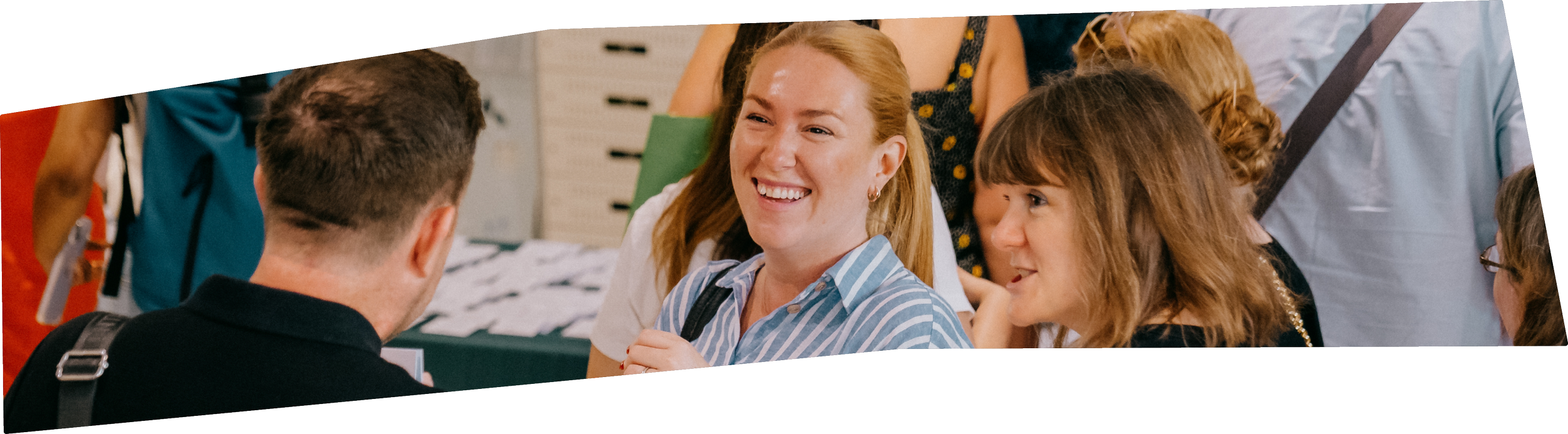People at a registration or check-in desk, engaging in conversation, with a smiling woman and a girl in the foreground, and others in the background.