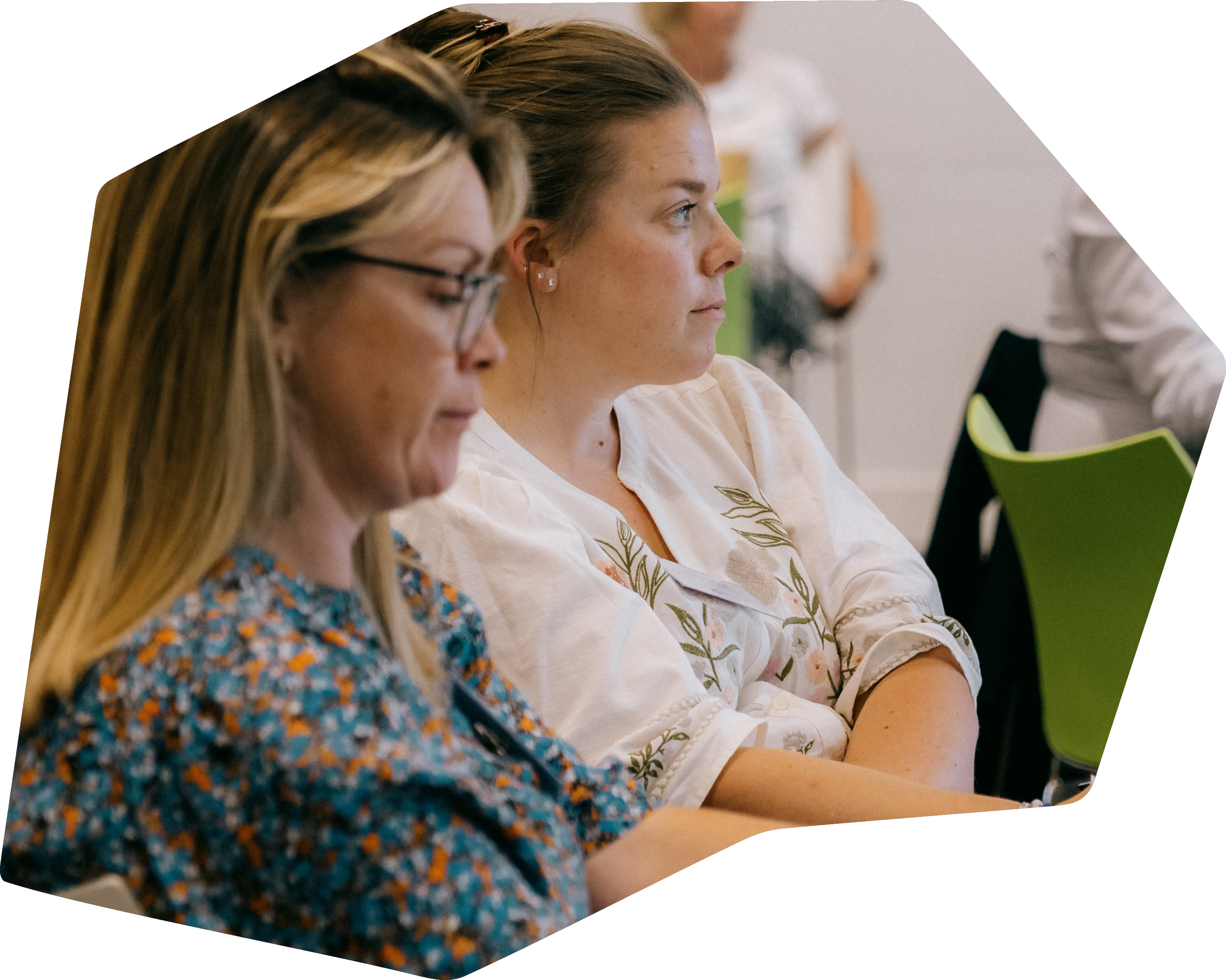 Two women sitting in a meeting room, attentively listening.