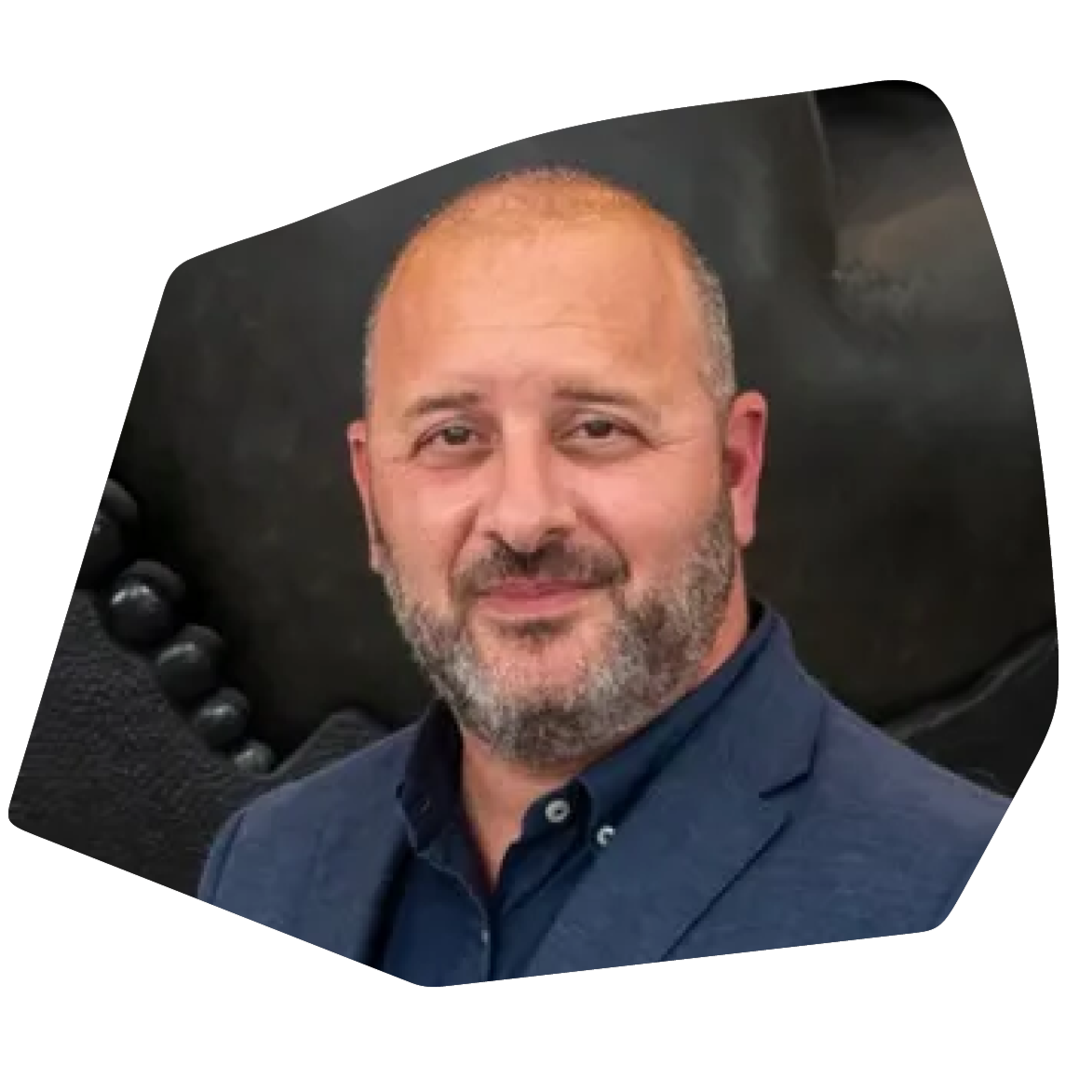 Portrait of a middle-aged man with a beard, wearing a navy blue blazer and shirt, smiling at the camera.