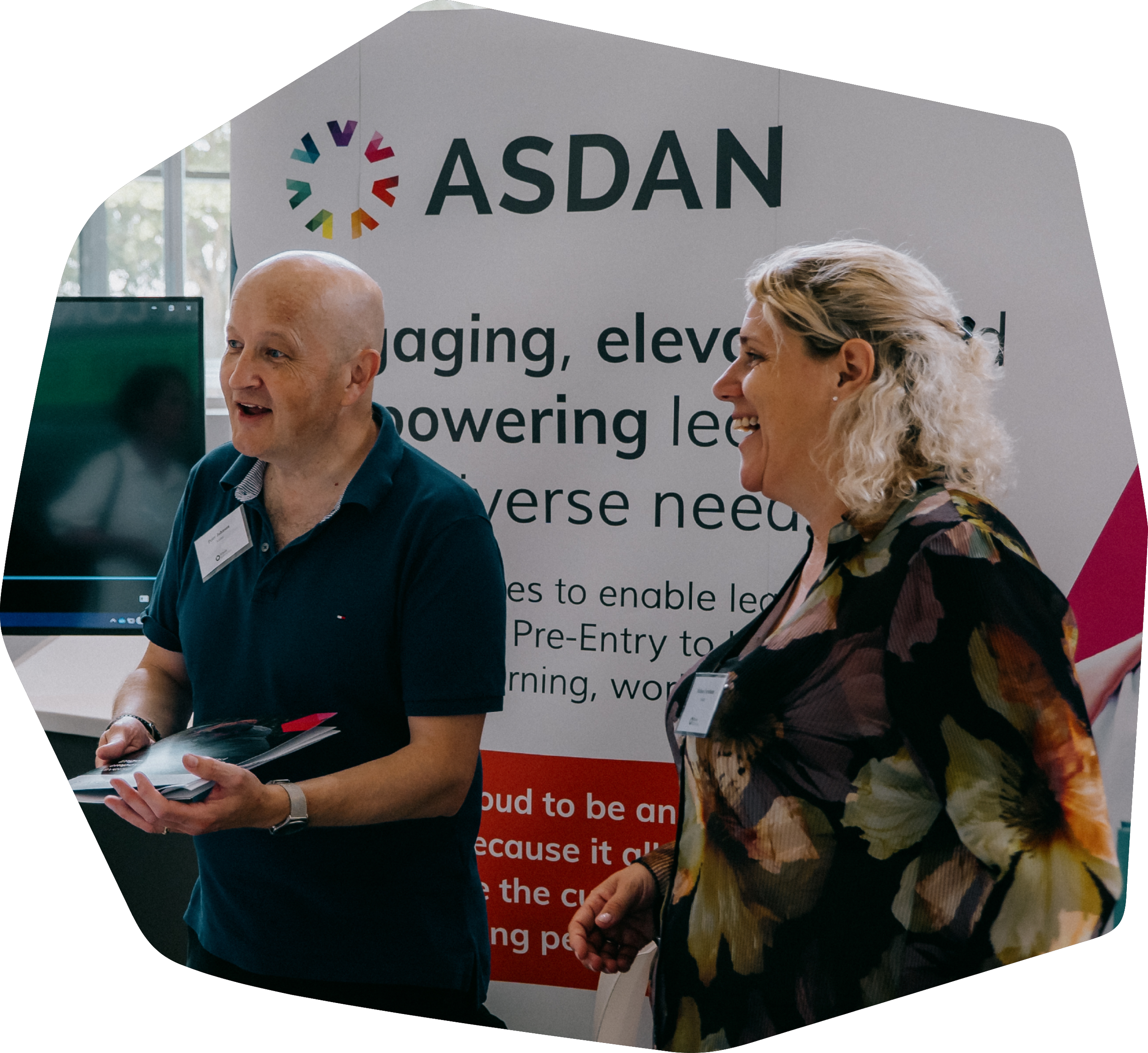 People at a conference booth talking and exchanging information, with a large banner that reads 'ASDAN' and shows an image of a smiling Black woman with a backpack.