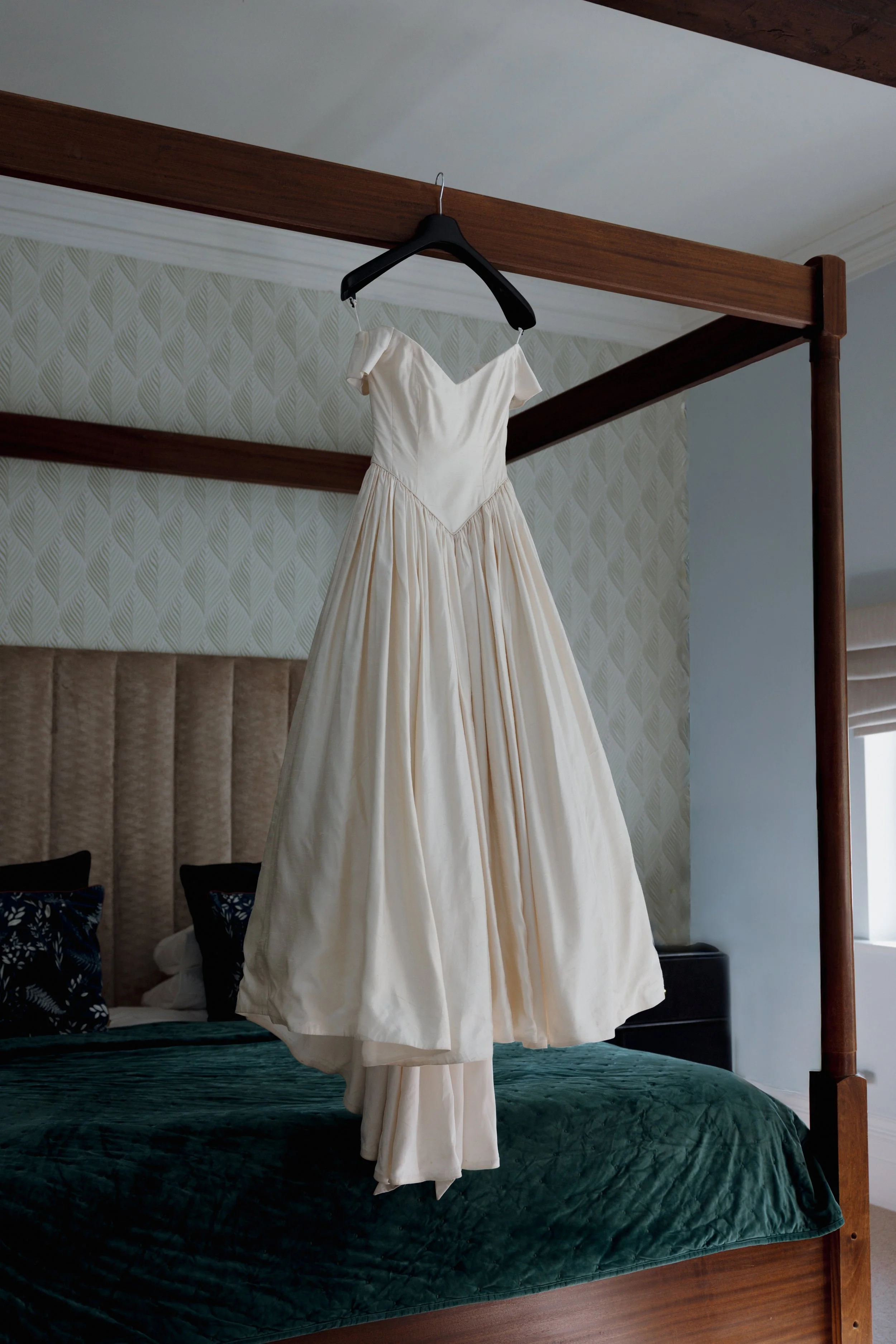 White dress hanging from a black hanger over a dark green bed in a bedroom