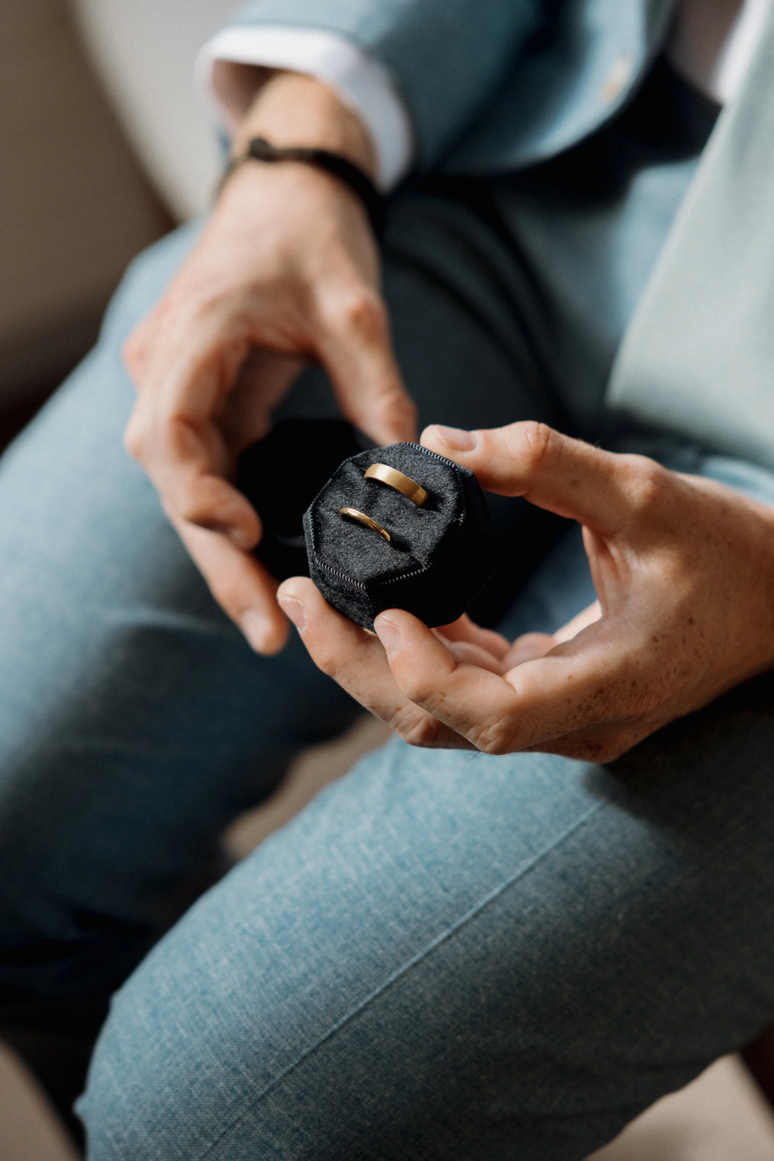 A person holding a small black jewelry box with gold rings inside.