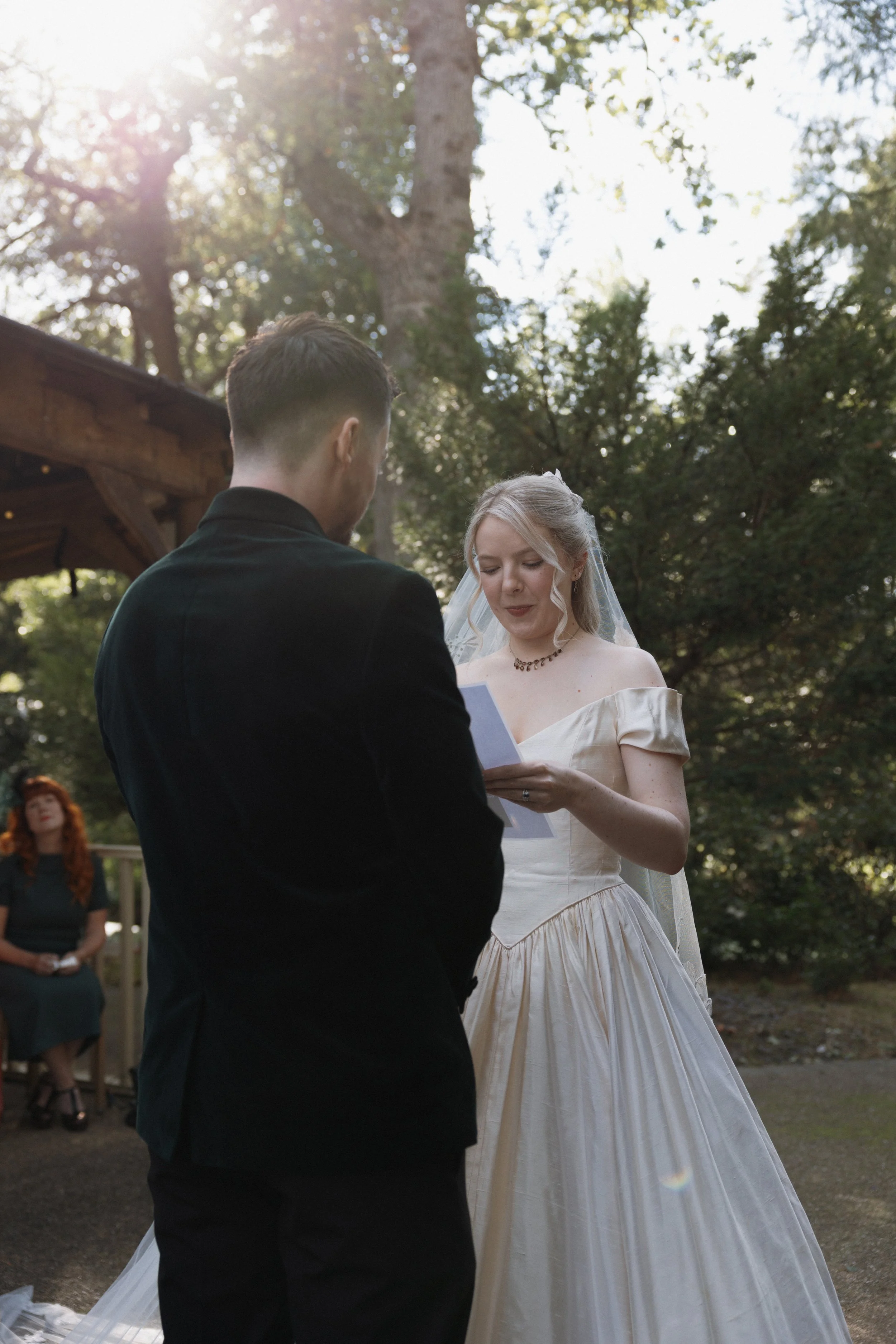 Bride reading vows to groom during an outdoor wedding ceremony in a wooded setting