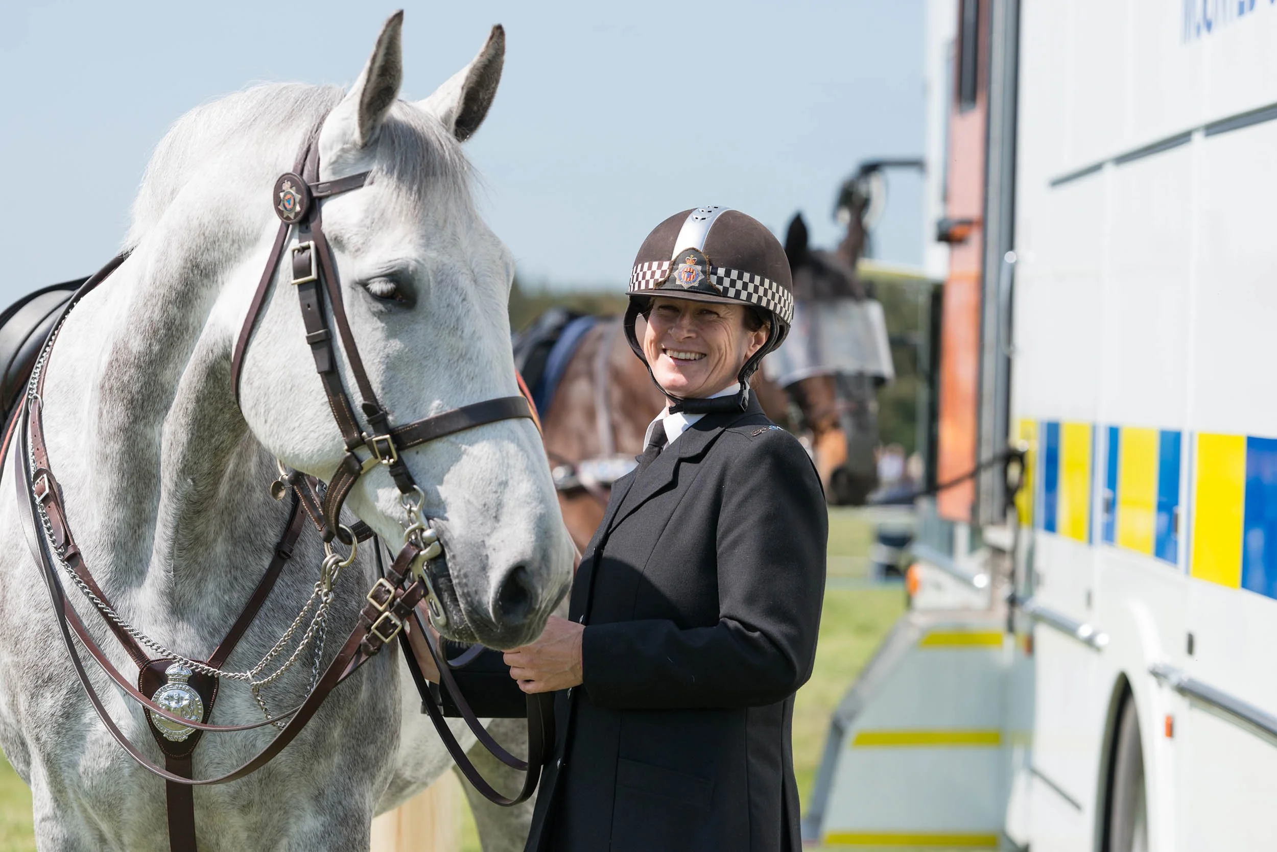 Image of a smiling police woman with her horse during the festival of the heavy horse at Etal in Northumberland. They getting ready to take part in the main ring, on a very bright and sunny morning .