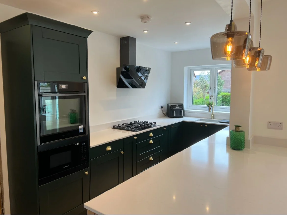 Modern kitchen with black cabinetry, white countertops, a gas stove, a black microwave, a window with a view of greenery, and pendant lighting.