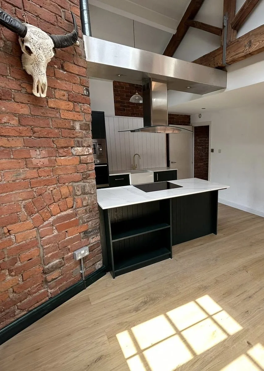 Modern kitchen with red exposed brick wall, black cabinetry, white Calacatta Oro, stainless steel range hood, and a skull of an animal with horns mounted on the brick wall.