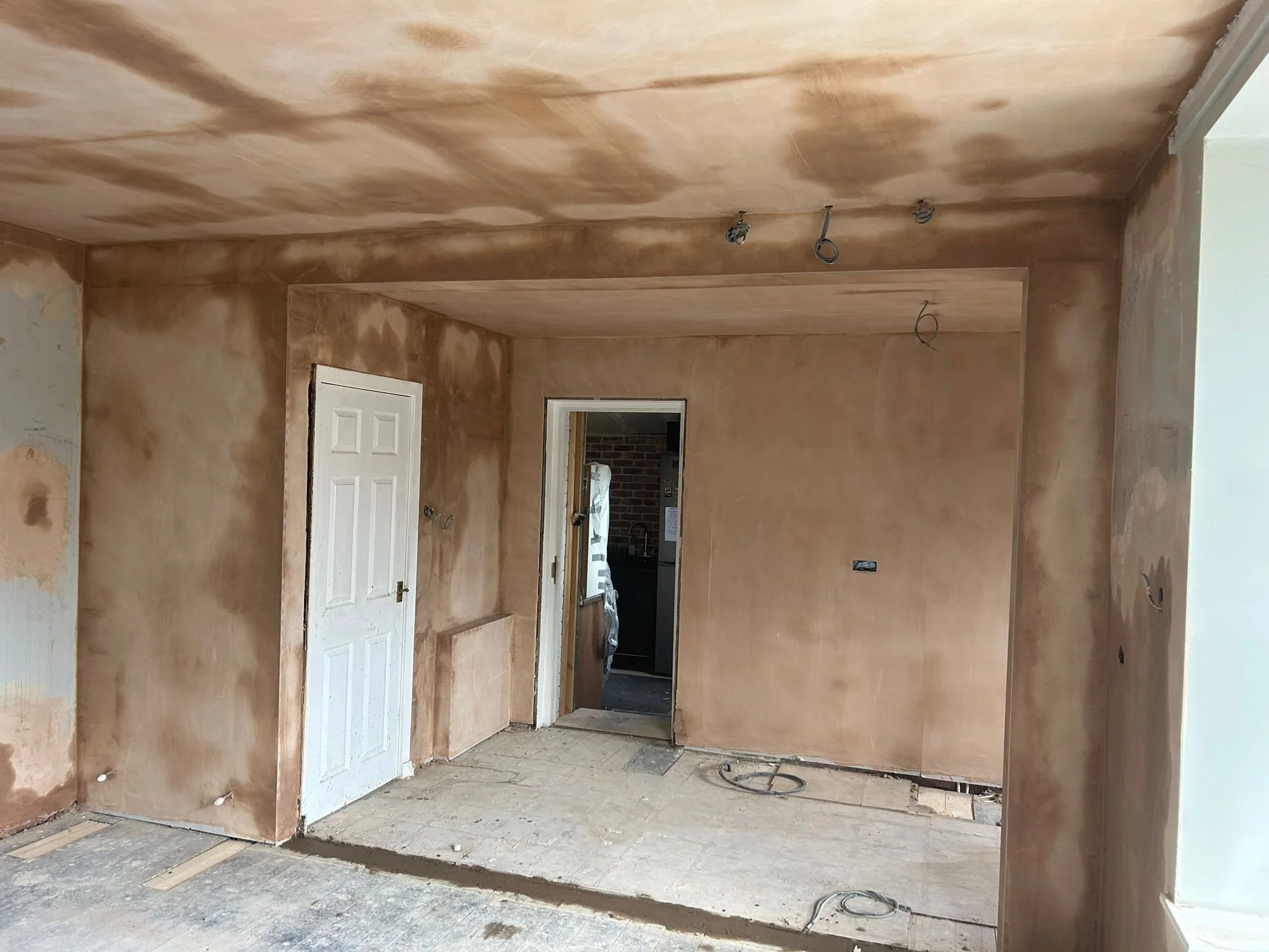 Room under construction with unpainted walls and ceiling, holes for electrical wiring, and exposed flooring.