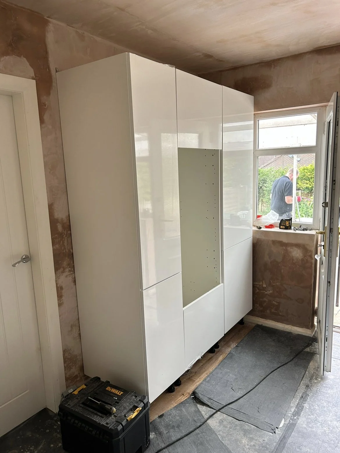 A partially assembled white cabinet next to a window in a room under renovation.