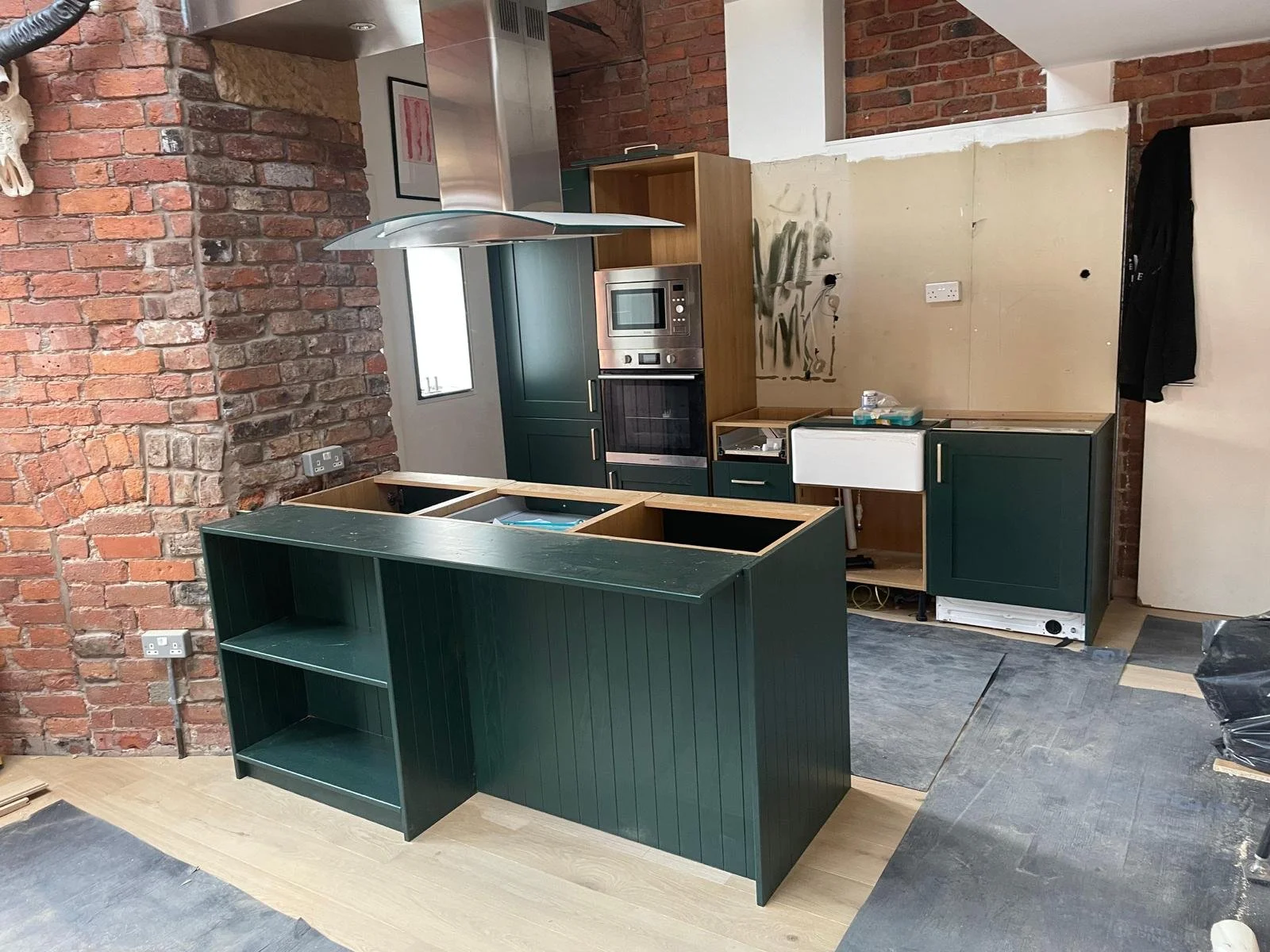 Kitchen under renovation with green cabinets, brick wall, and construction materials.