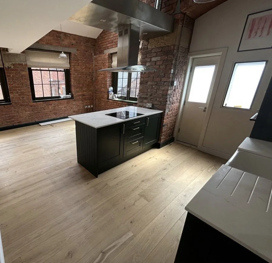 Modern kitchen with brick walls, wooden flooring, black island with white countertop, and stainless steel range hood.