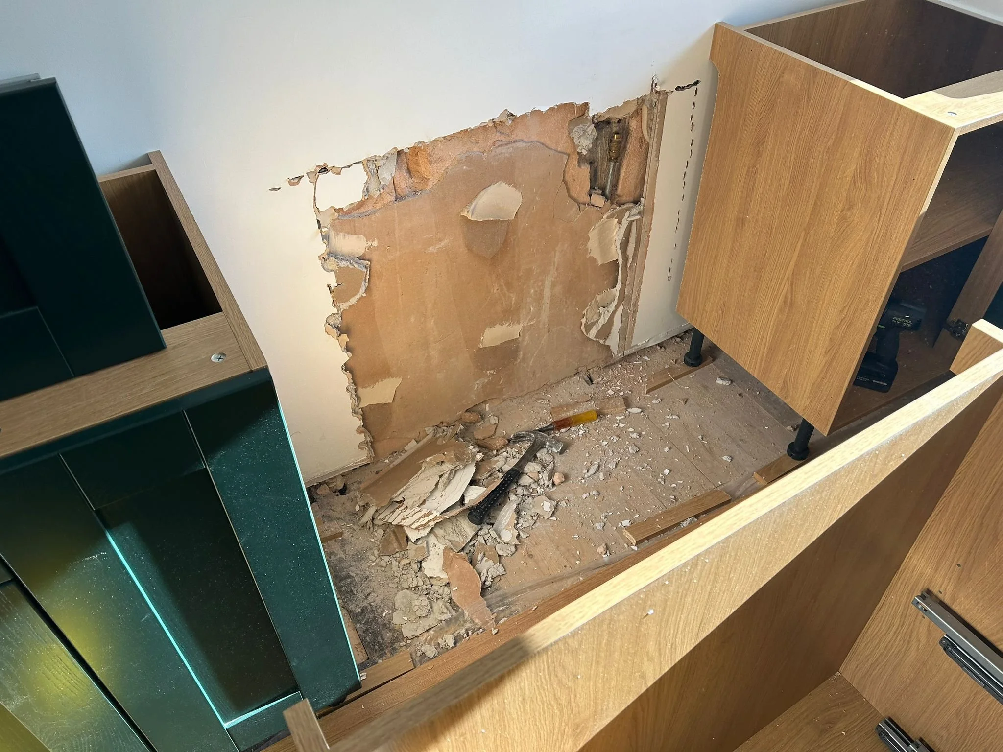 Kitchen with a removed cabinet, exposing a wall with damaged drywall and insulation, debris on the floor, and several tools scattered around.