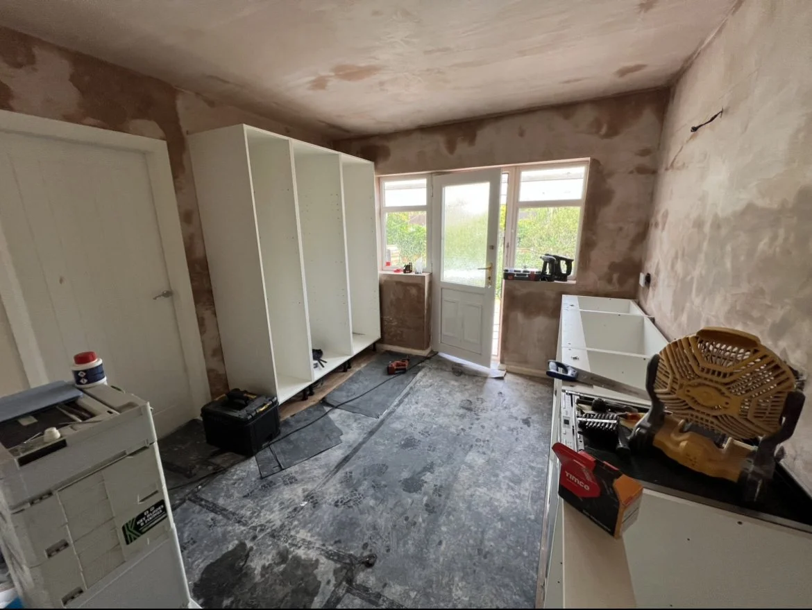 Room under renovation with exposed walls, partially installed white cabinets, construction tools, and a door leading outside.