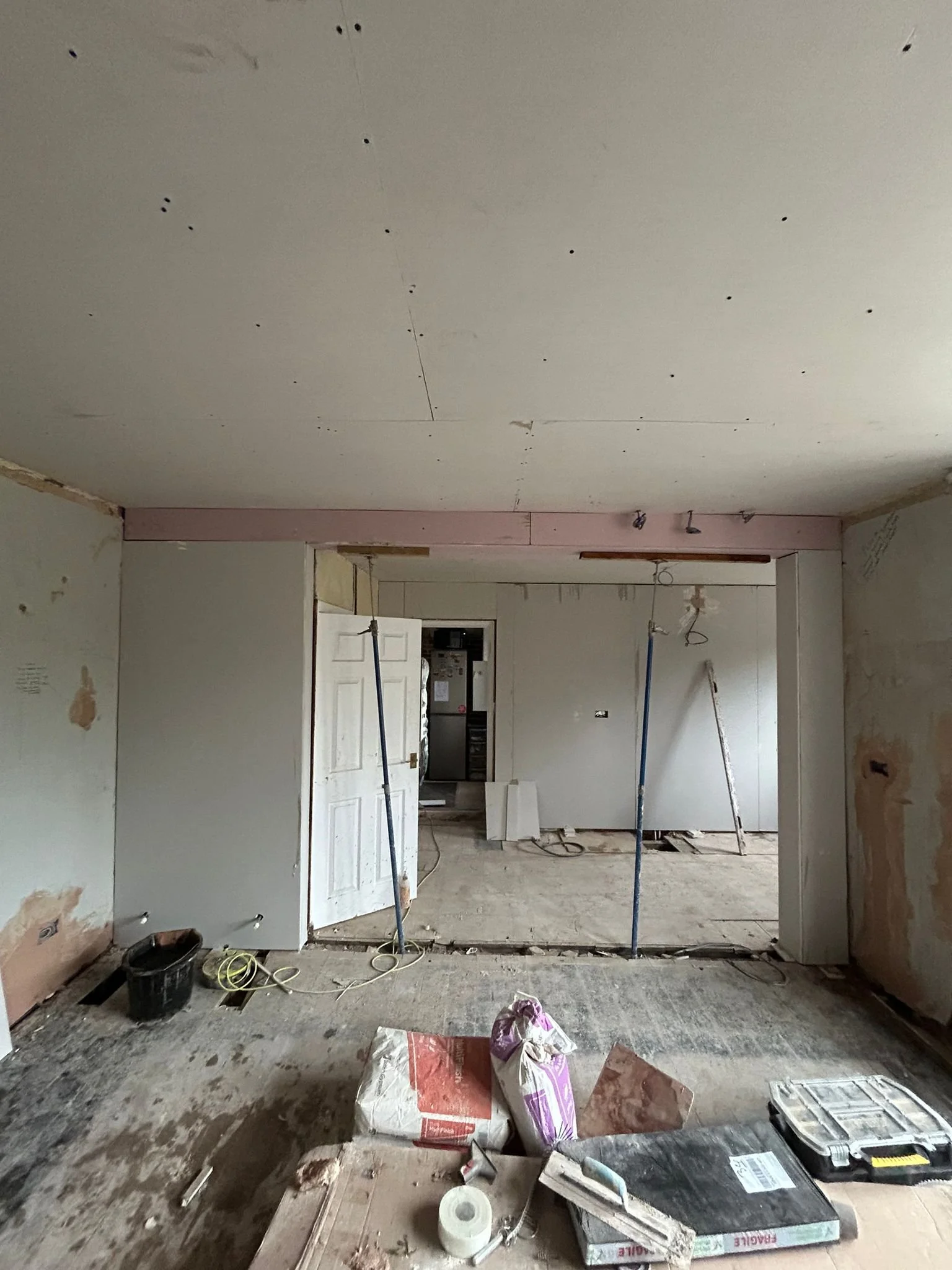 Interior of a room under renovation with unfinished walls and ceiling, construction tools, materials, and debris on the floor.