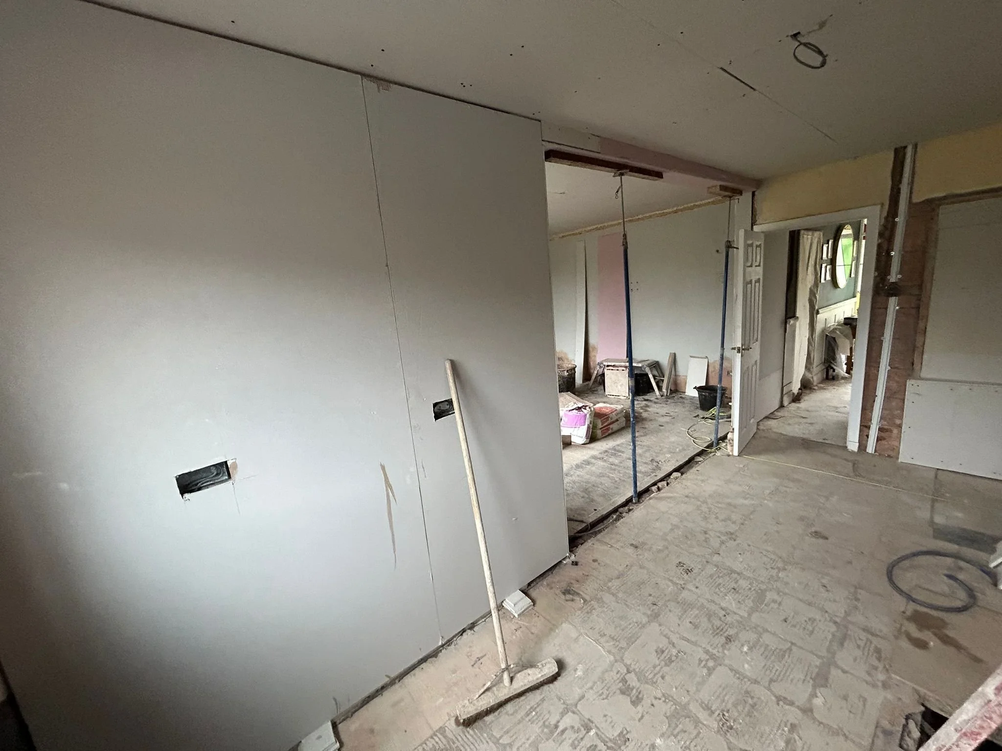 Interior of a house under renovation with drywall, construction tools, and supplies scattered on the floor.