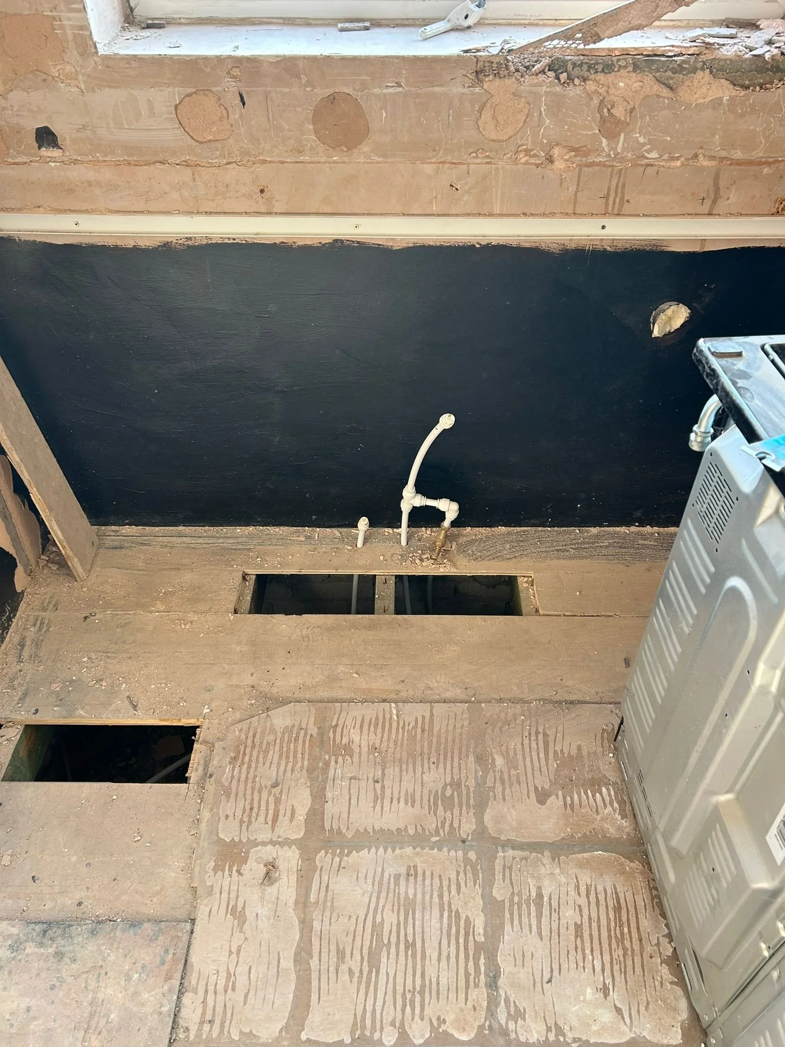 A partially constructed or renovated bathroom with exposed wood flooring, a black painted wall, a plumbing pipe, and a utility heater or air conditioning unit on the right side.