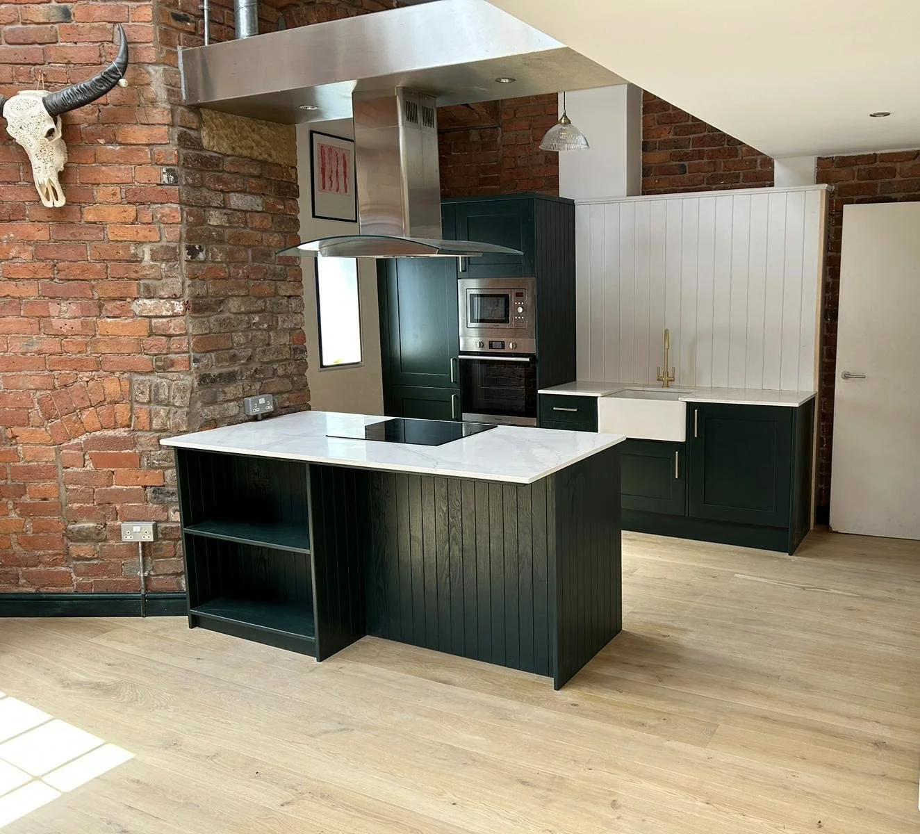 Modern kitchen with dark green cabinets, white quartz worktops, brick walls, and a black kitchen island with open shelving.