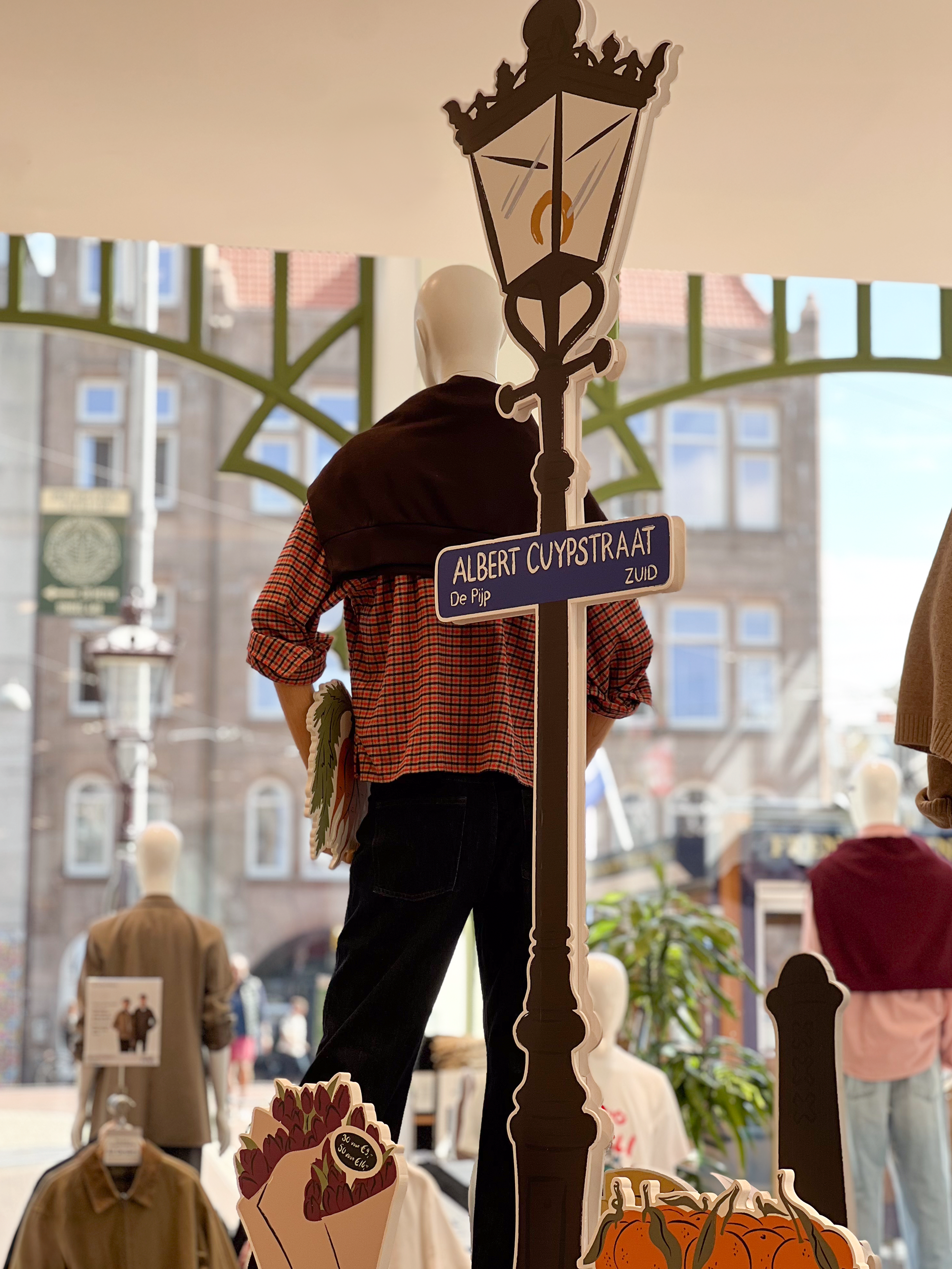 Illustrated prop of a lantern featuring an Albert Cuypstraat street sign, placed next to a mannequin, designed by Sandy van Helden for UNIQLO Koningsplein’s autumn 2025 market-themed visual merchandising.
