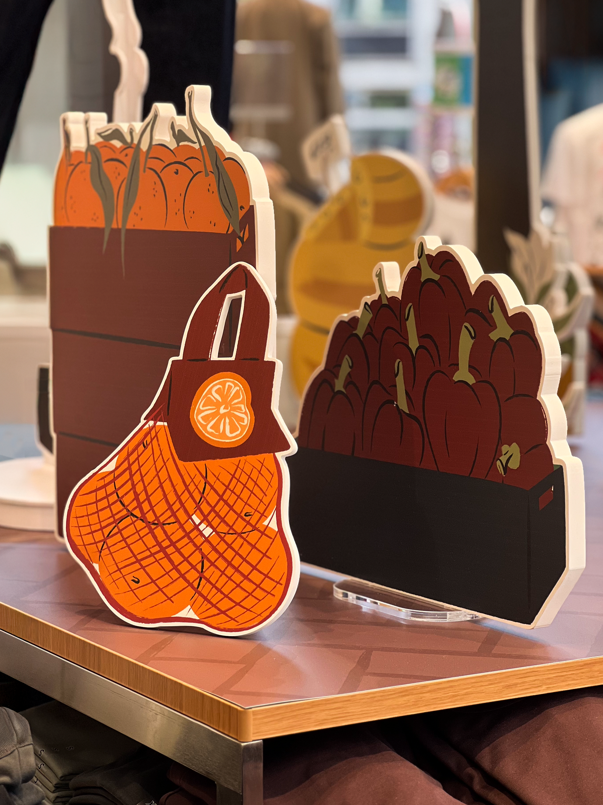 Illustrated props of crates filled with oranges and bell pepers, and in front a new with oranges, illustrated by Sandy van Helden, as part of UNIQLO's Koningsplein’s autumn 2025 visual merchandising.