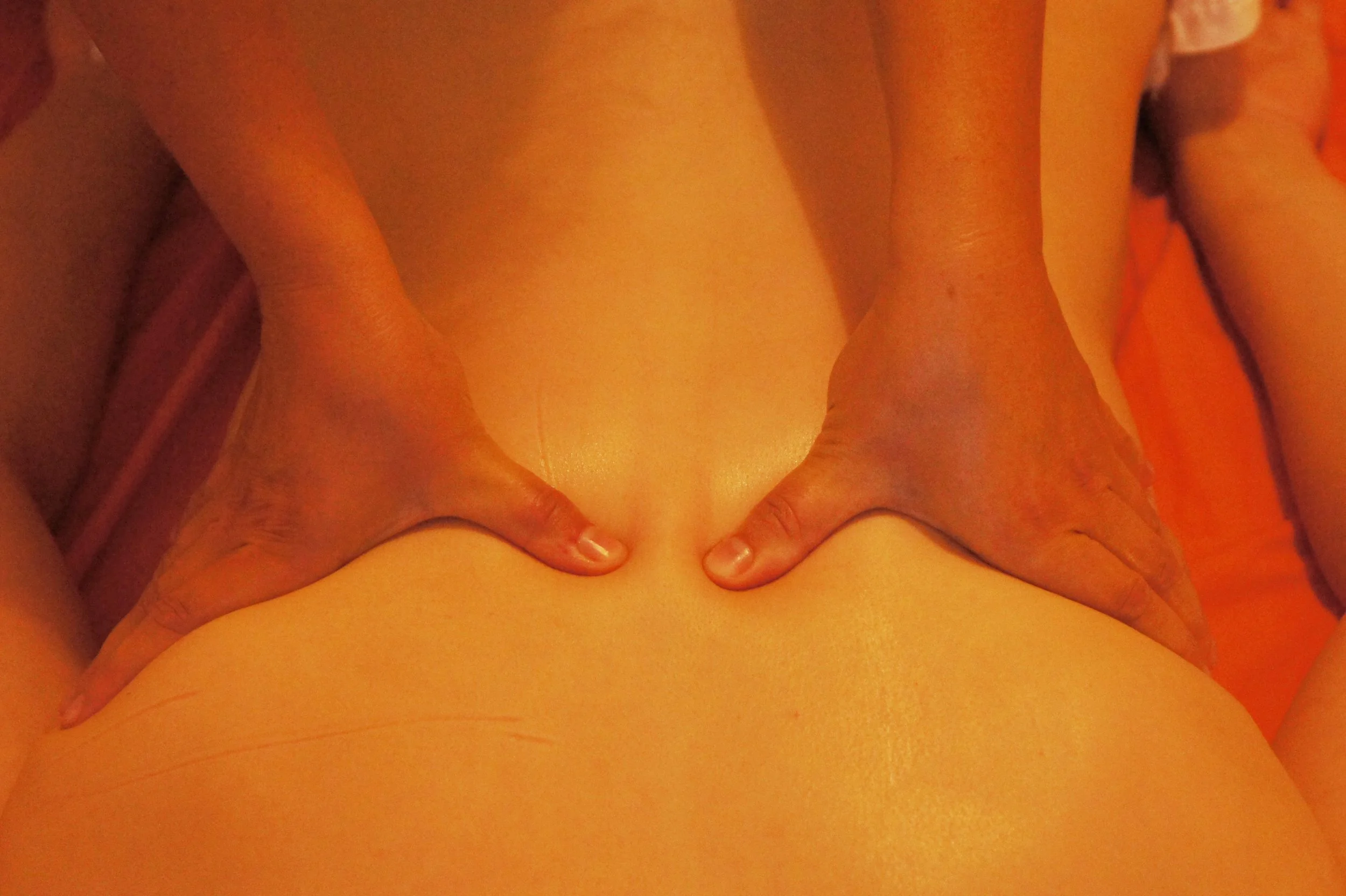 Nahaufnahme eines Rückens, der gerade massiert wird, mit Fokus auf den unteren Rücken, in warmem Licht.