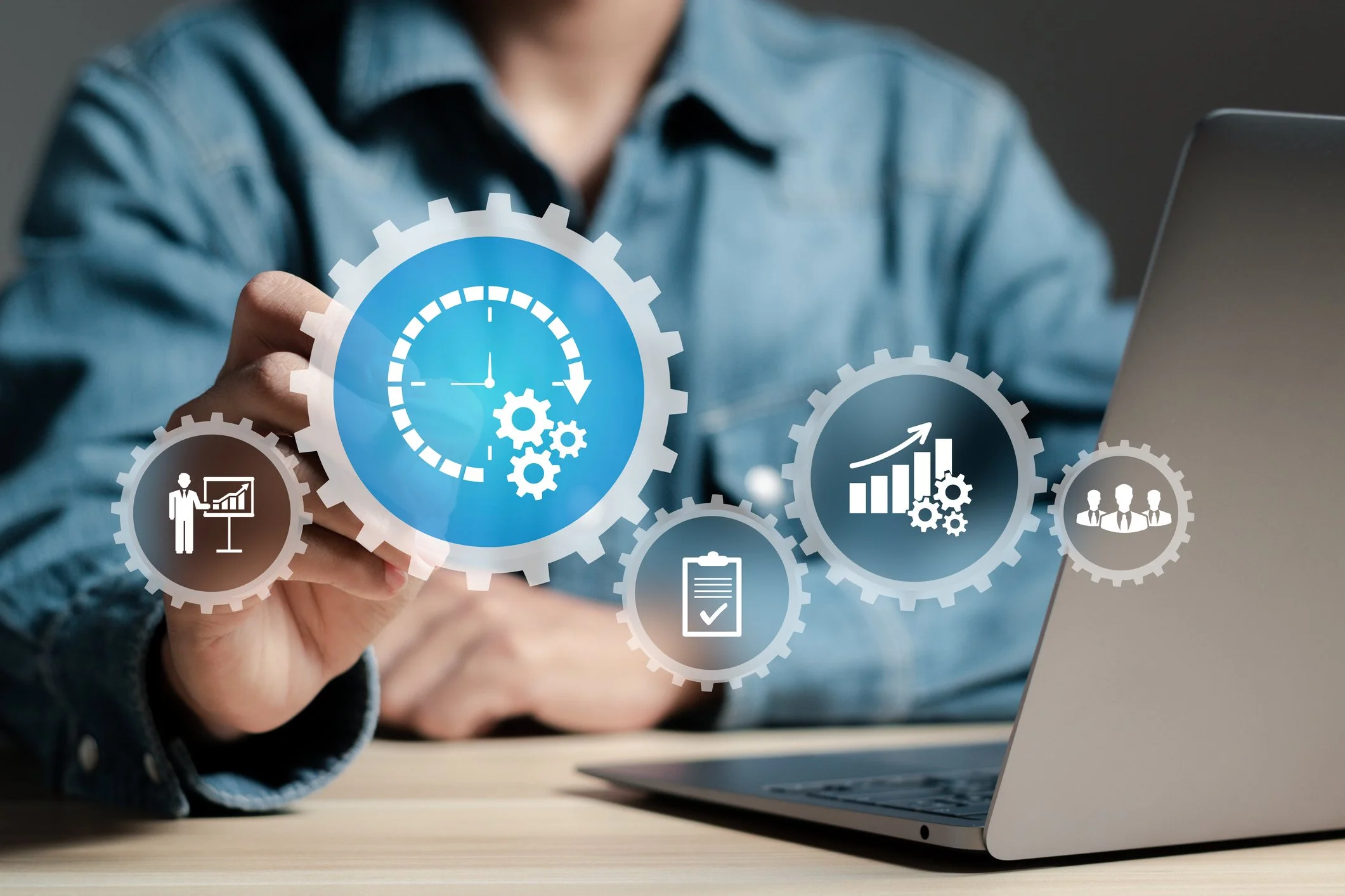Person using a laptop with overlay icons of gears, charts, clipboard, and people representing business and productivity concepts.