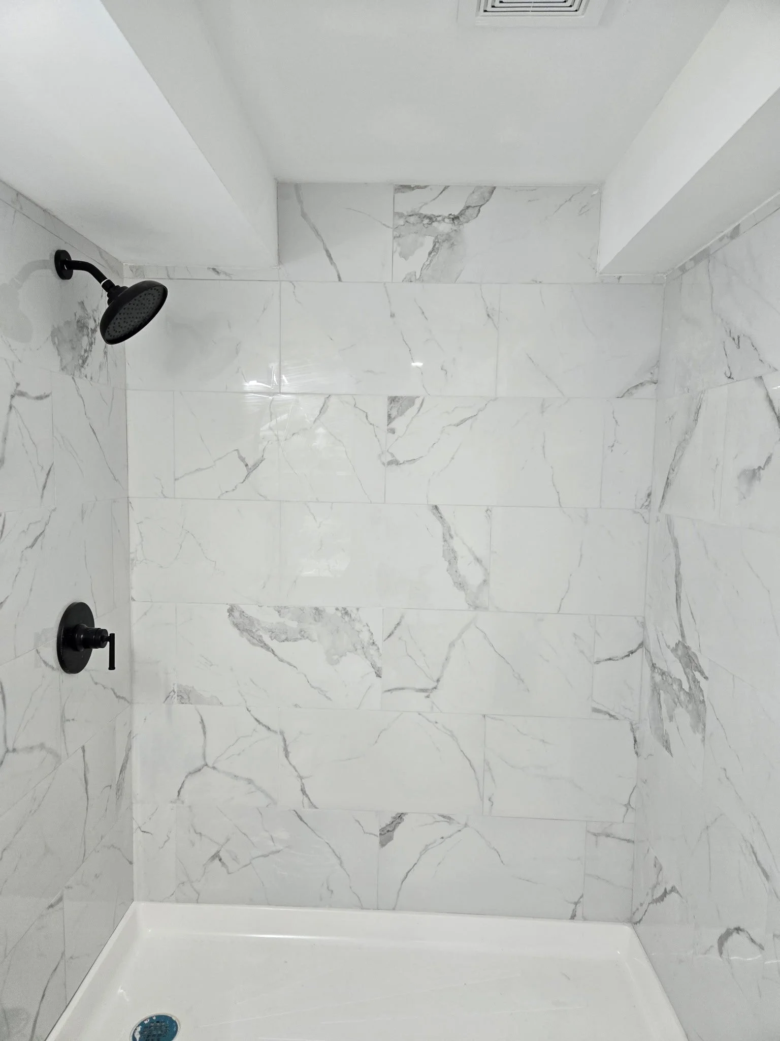 Empty walk-in shower with white marble tiles, black showerhead, and black control handle.