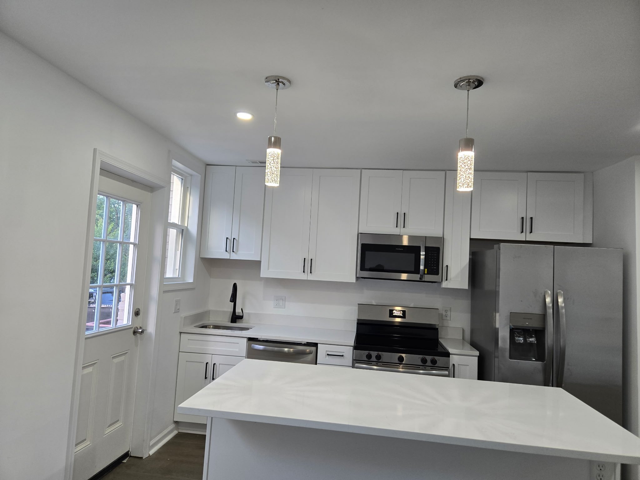 Modern kitchen with white cabinets, stainless steel appliances, pendant lights, a window, and a central island.
