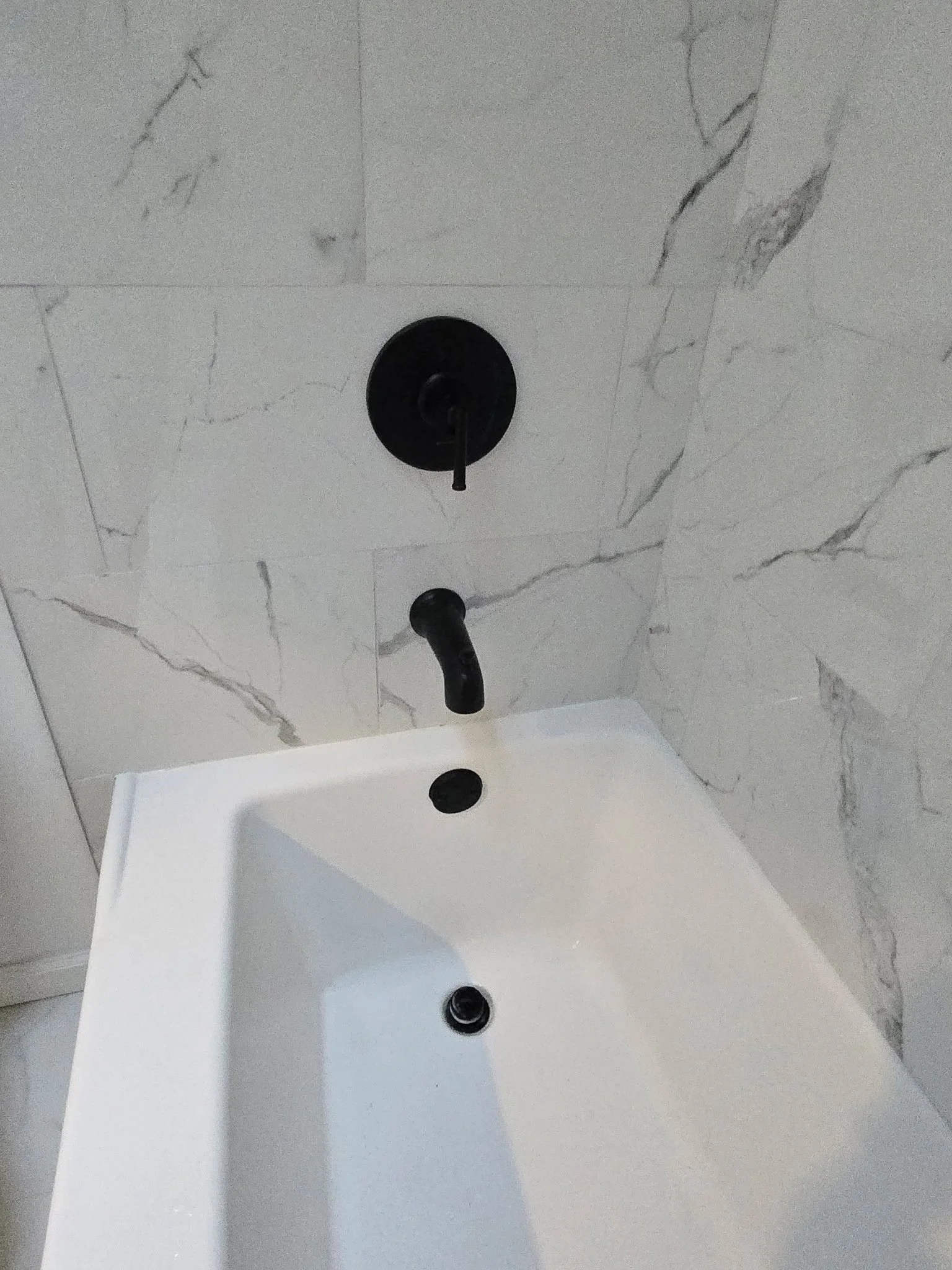 Close-up of a bathroom sink with black faucet and handles, marble patterned wall tiles, and a white basin.