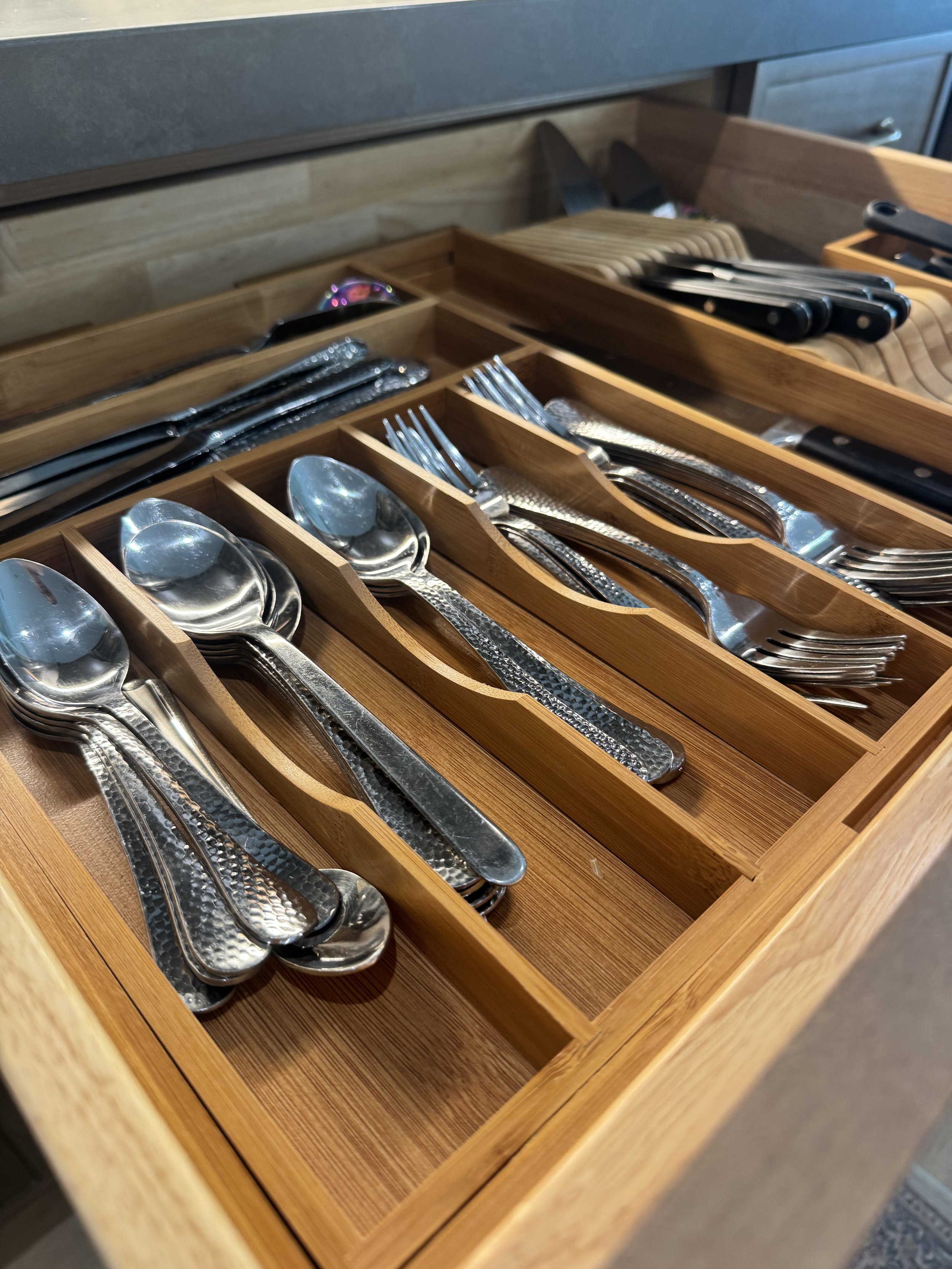Wooden drawer with organized silverware, including spoons and forks.