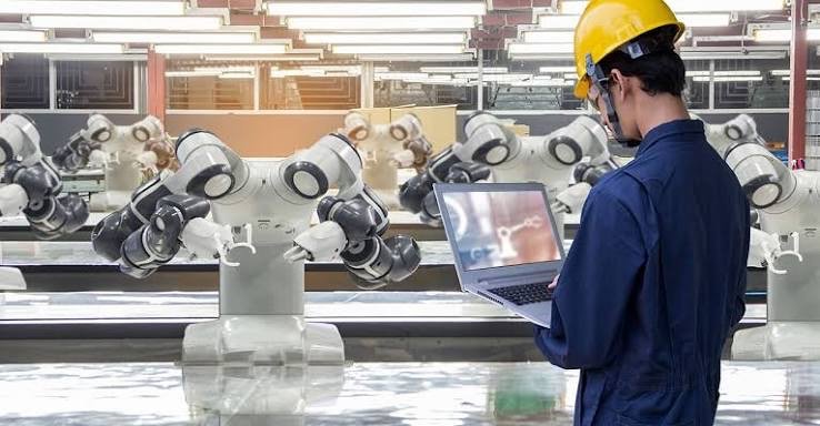 Engineer in a hard hat inspecting automated equipment with a tablet