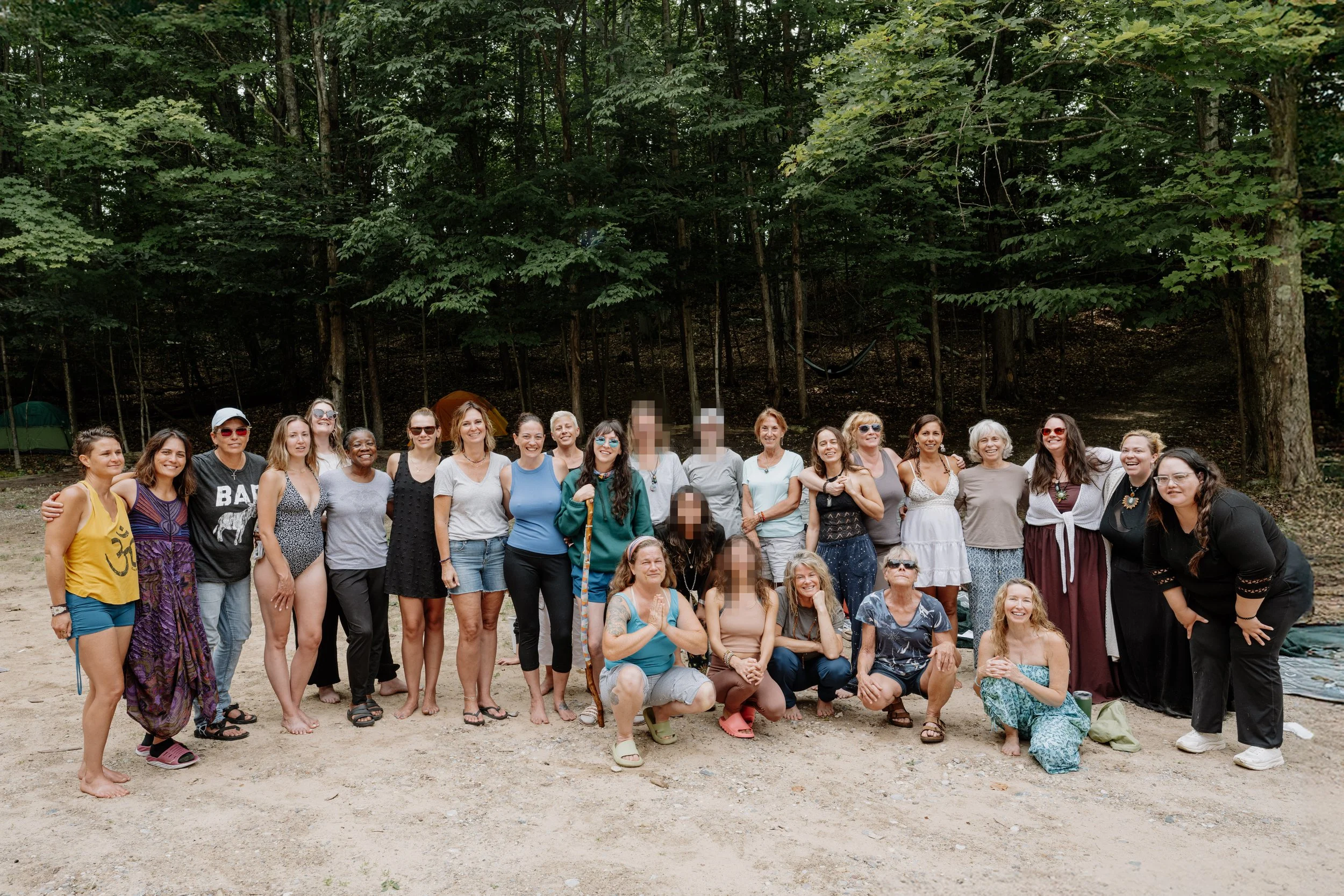 A group of around 20 women gathered outdoors on a dirt surface in front of a wooded area, posing for a photo together at the end of an all womens ayahuasca retreat