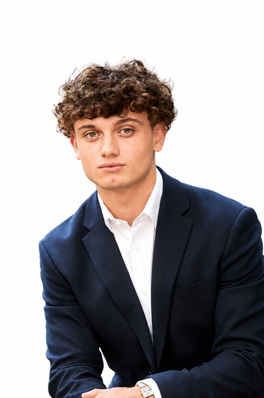 Portrait of a young man with curly brown hair, wearing a navy blazer and white shirt, against a plain white background.