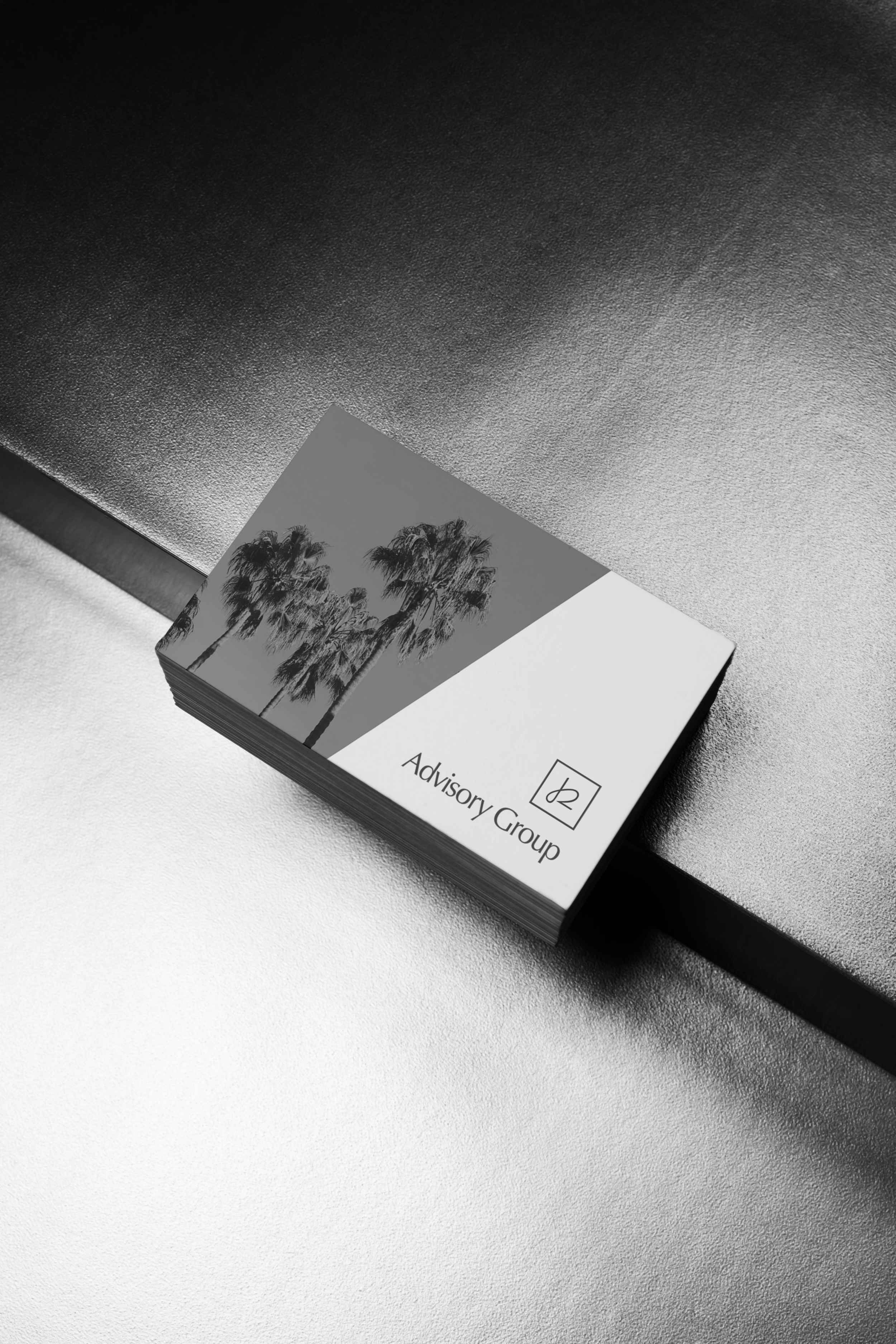 Stack of business cards with palm trees and 'Advisory Group' printed on them, placed on a reflective surface.