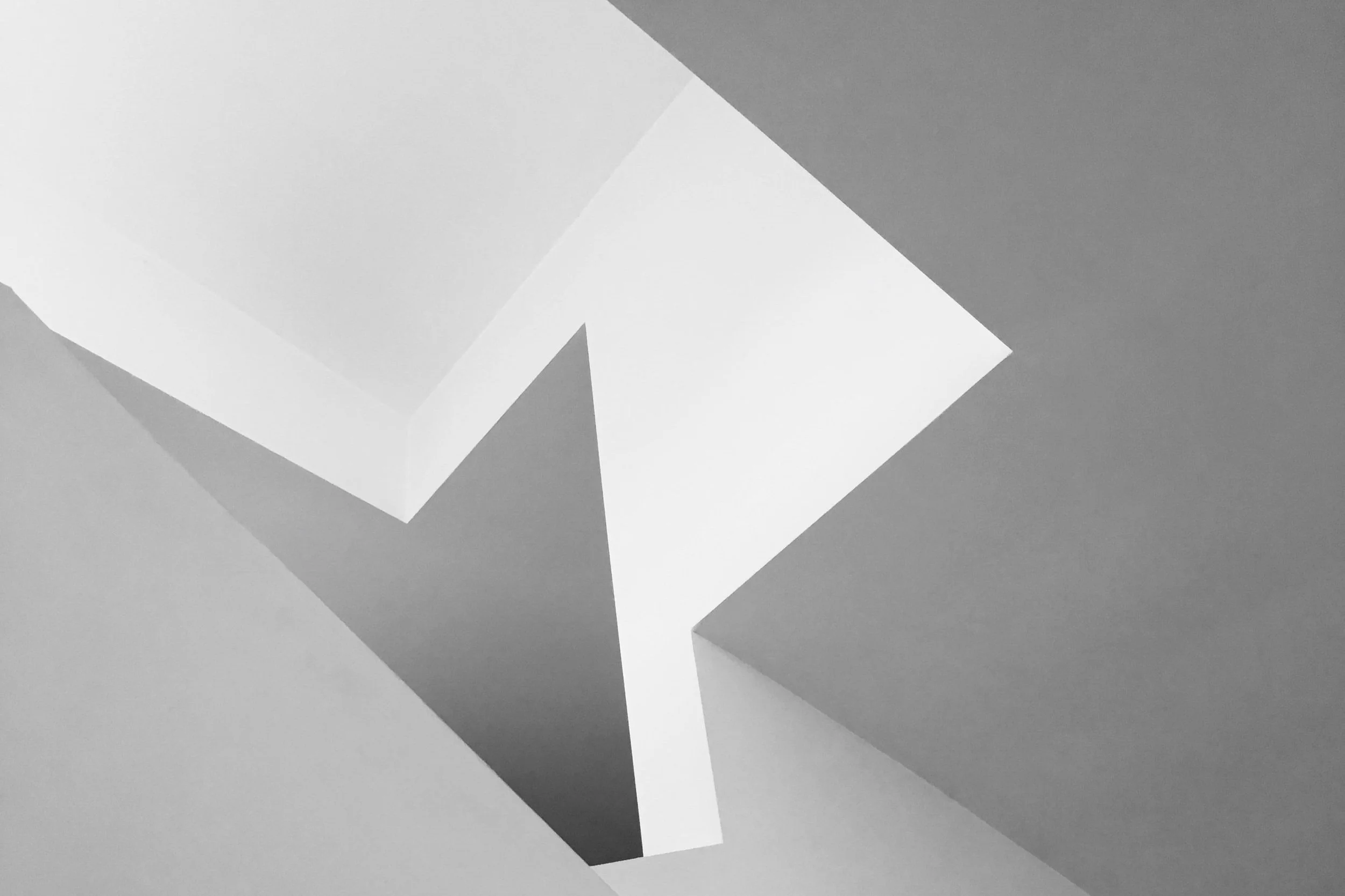 Close-up of a modern white geometric ceiling light fixture with angular design, surrounded by white ceiling panels.