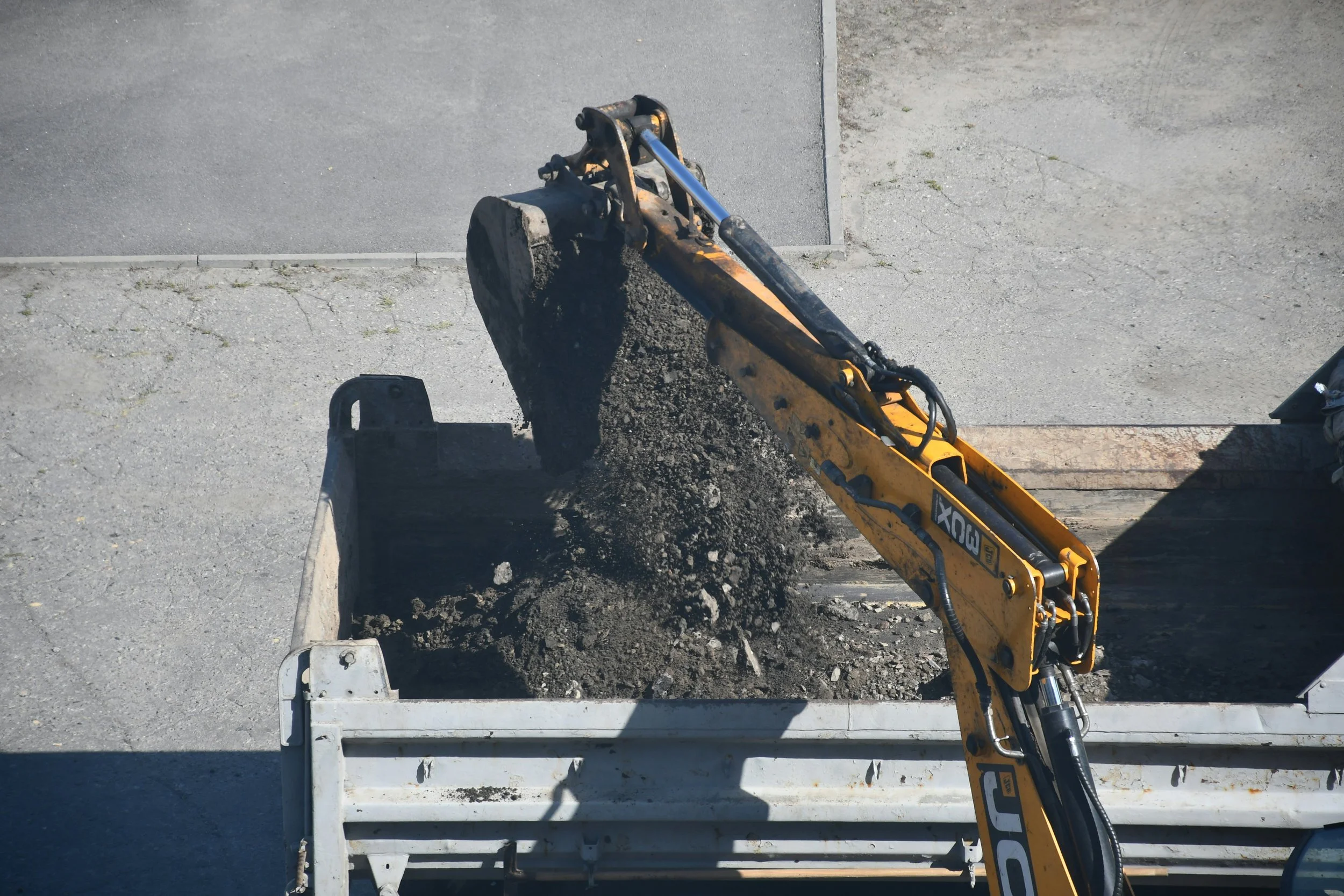 Baggerarm verlädt Aushub und Erde auf LKW für Gartenneugestaltung