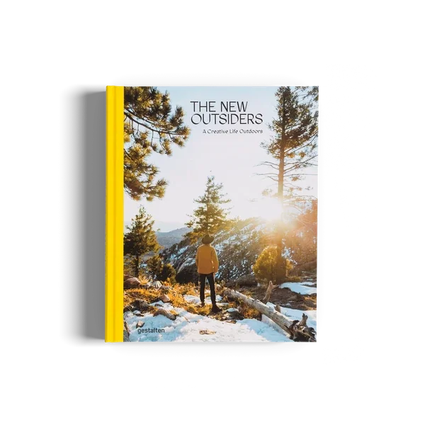 Book titled "The New Outsiders: A Creative Life Outdoors" featuring a person standing in a snow-covered forest with tall trees and sunlight shining through.