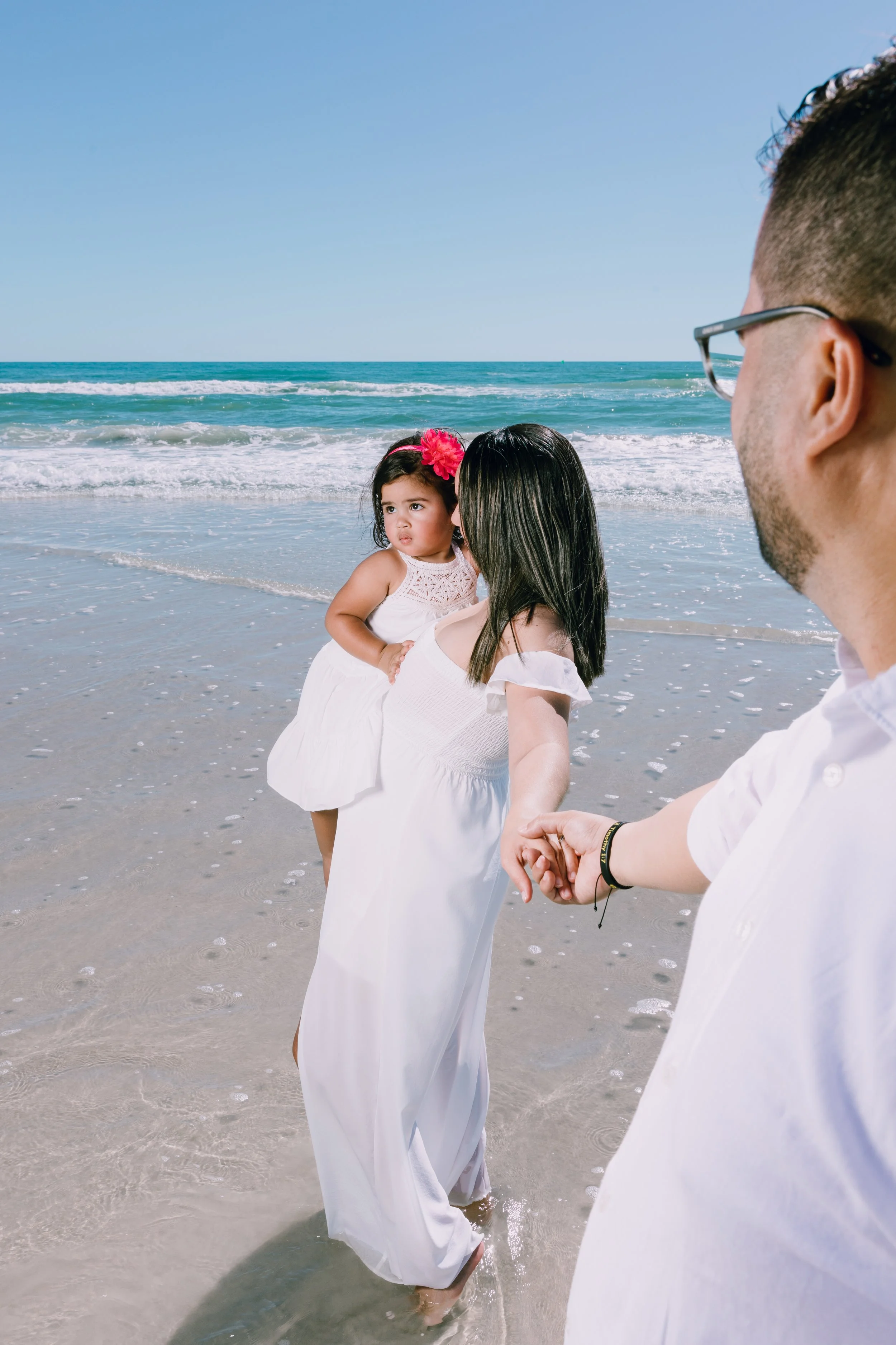 A woman holding a young girl at the beach while a man holds her hand.