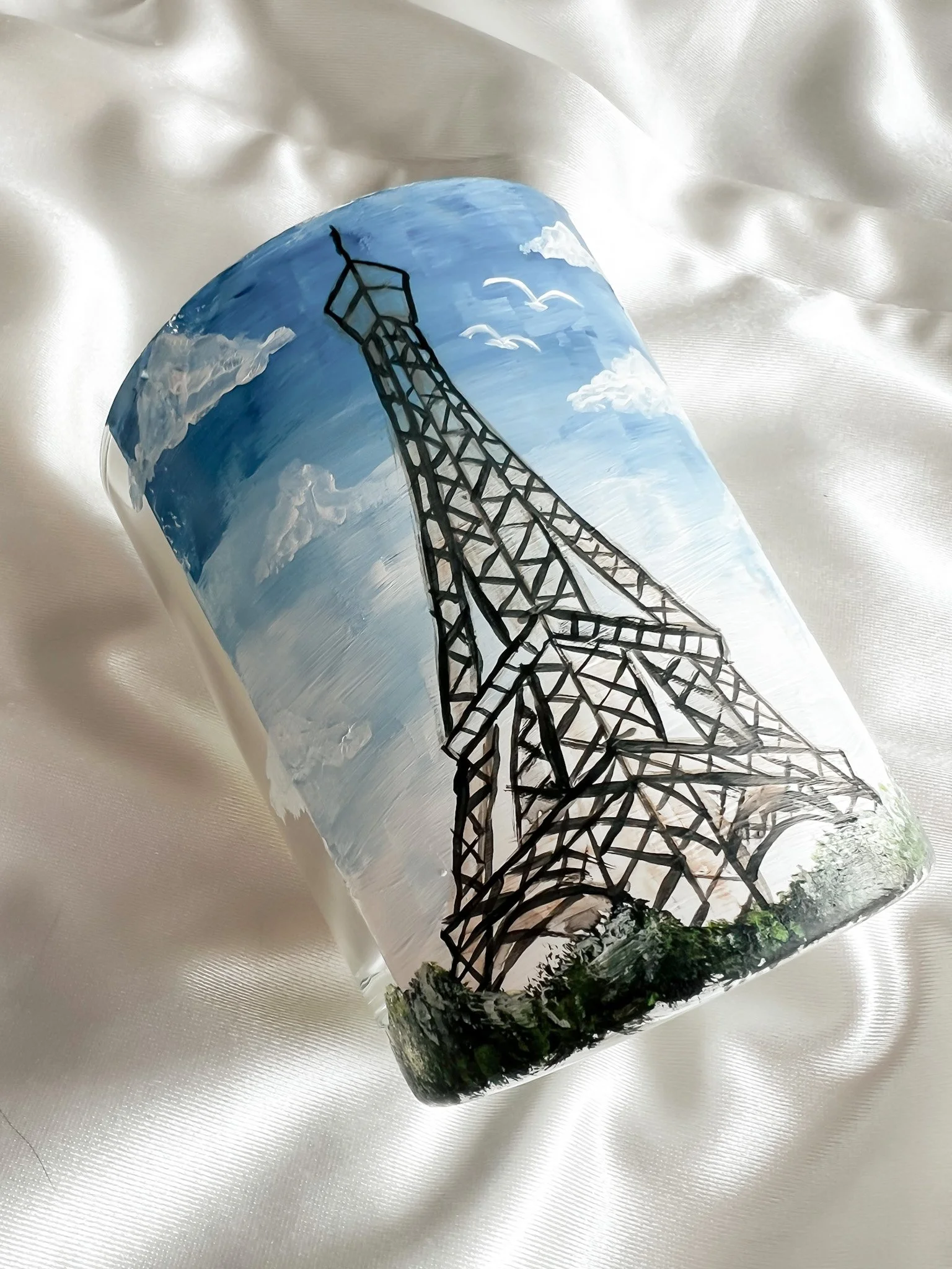 A painted glass featuring a black outline of a transmission tower set against a painted sky with clouds, birds, and a blue background.