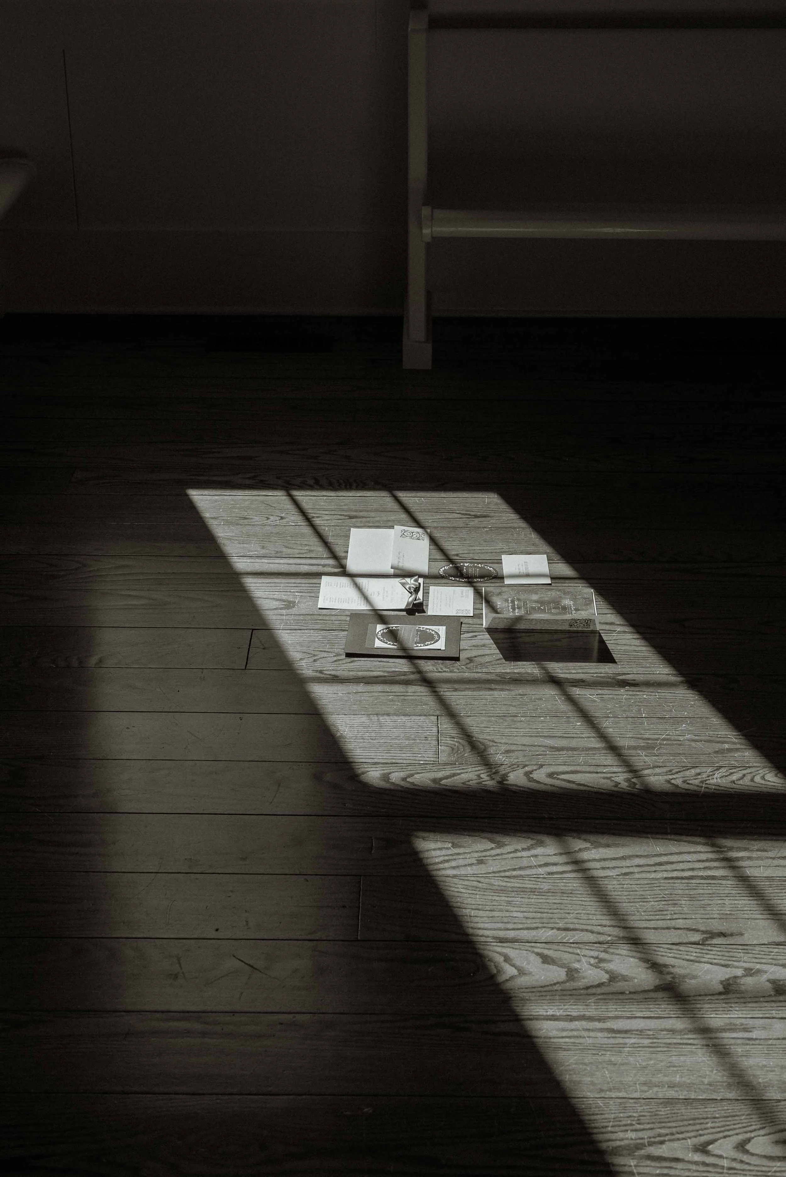 Sunlight casts shadows on wooden floor, illuminating papers, and a small box with objects inside.