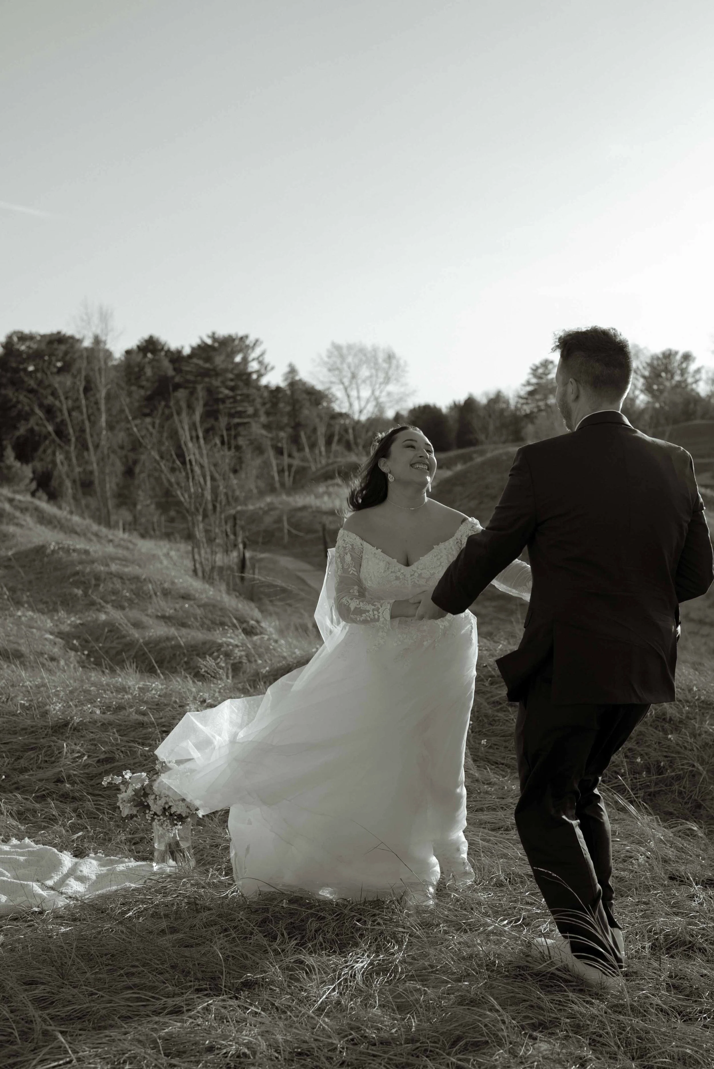 A bride and groom holding hands outdoors, with trees in the background, celebrating their wedding.