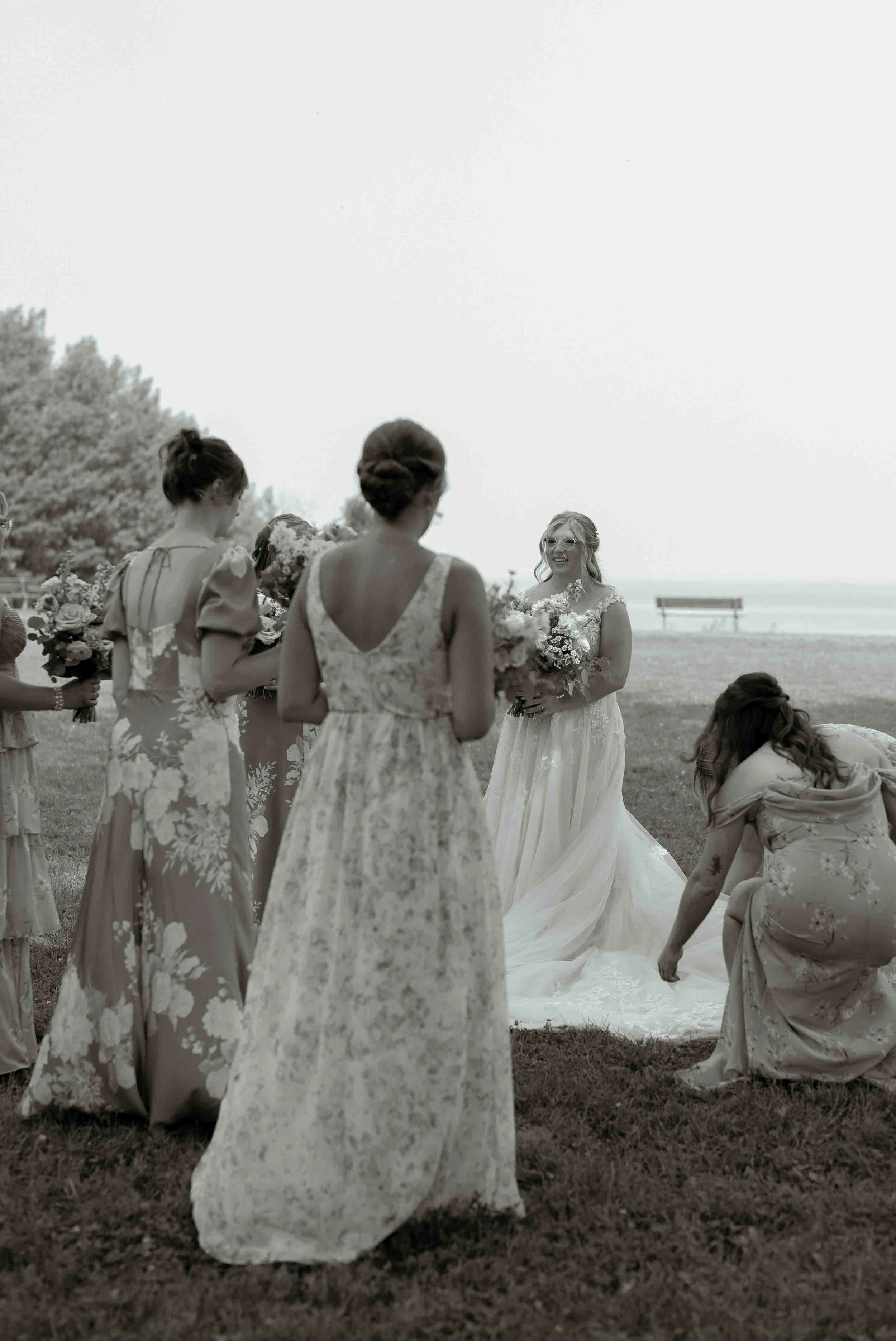 A wedding ceremony on a beach with women in floral dresses, a bride in a white gown, and people holding bouquets.