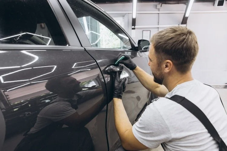 A man wearing a white shirt and gloves is painting a car with a brush, focused on achieving a smooth finish.