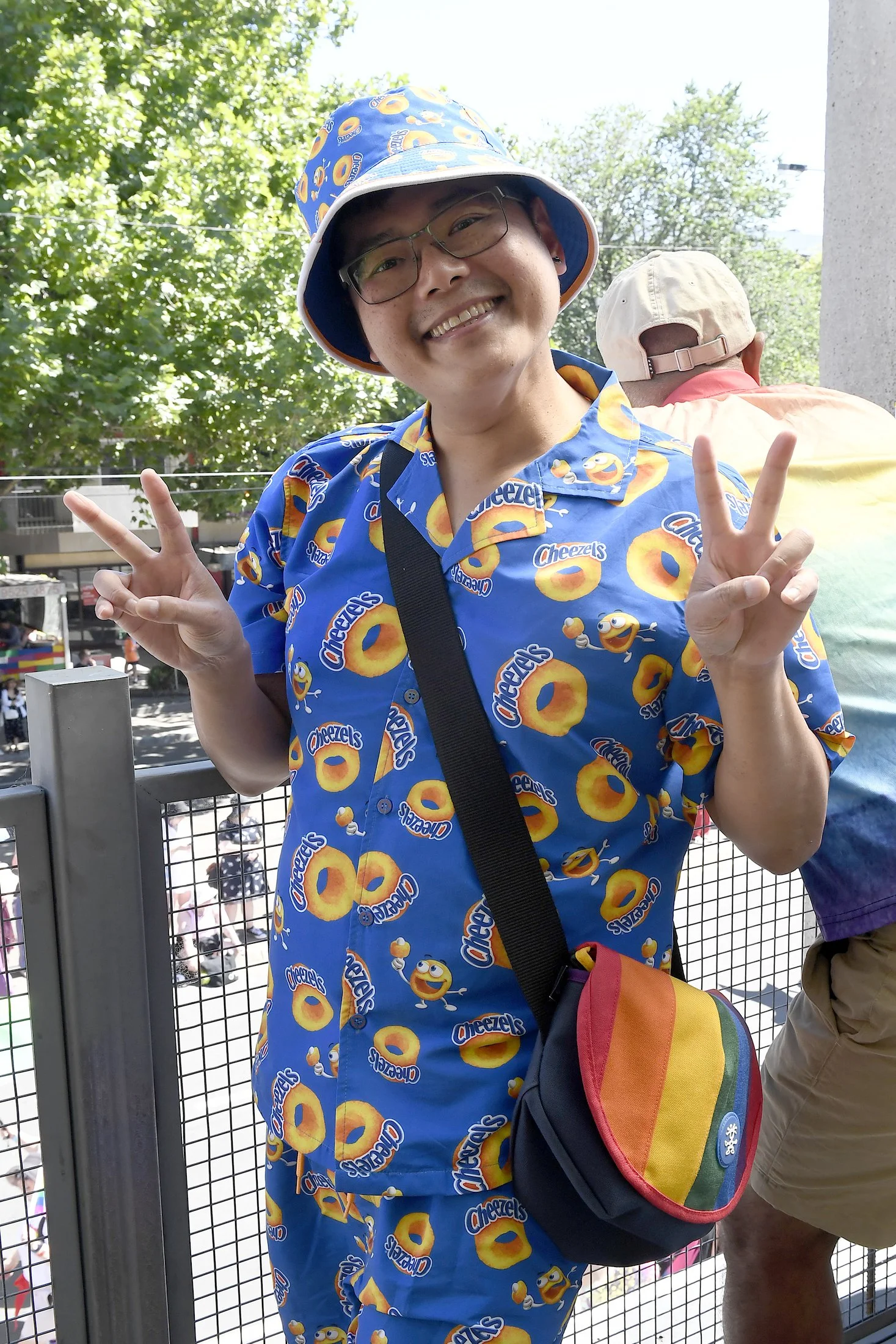 Person wearing a Cheezels-themed outfit and hat, smiling and making peace signs with both hands