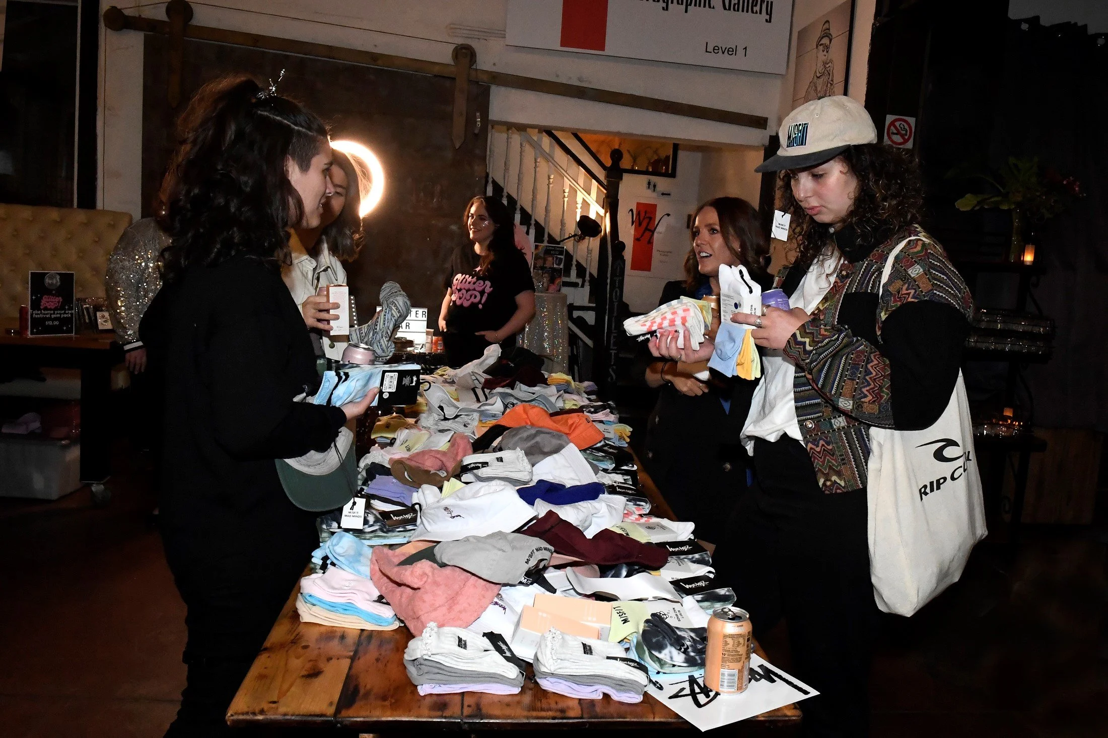Girls shopping at a table with clothes, shoes, and accessories in an indoor venue.