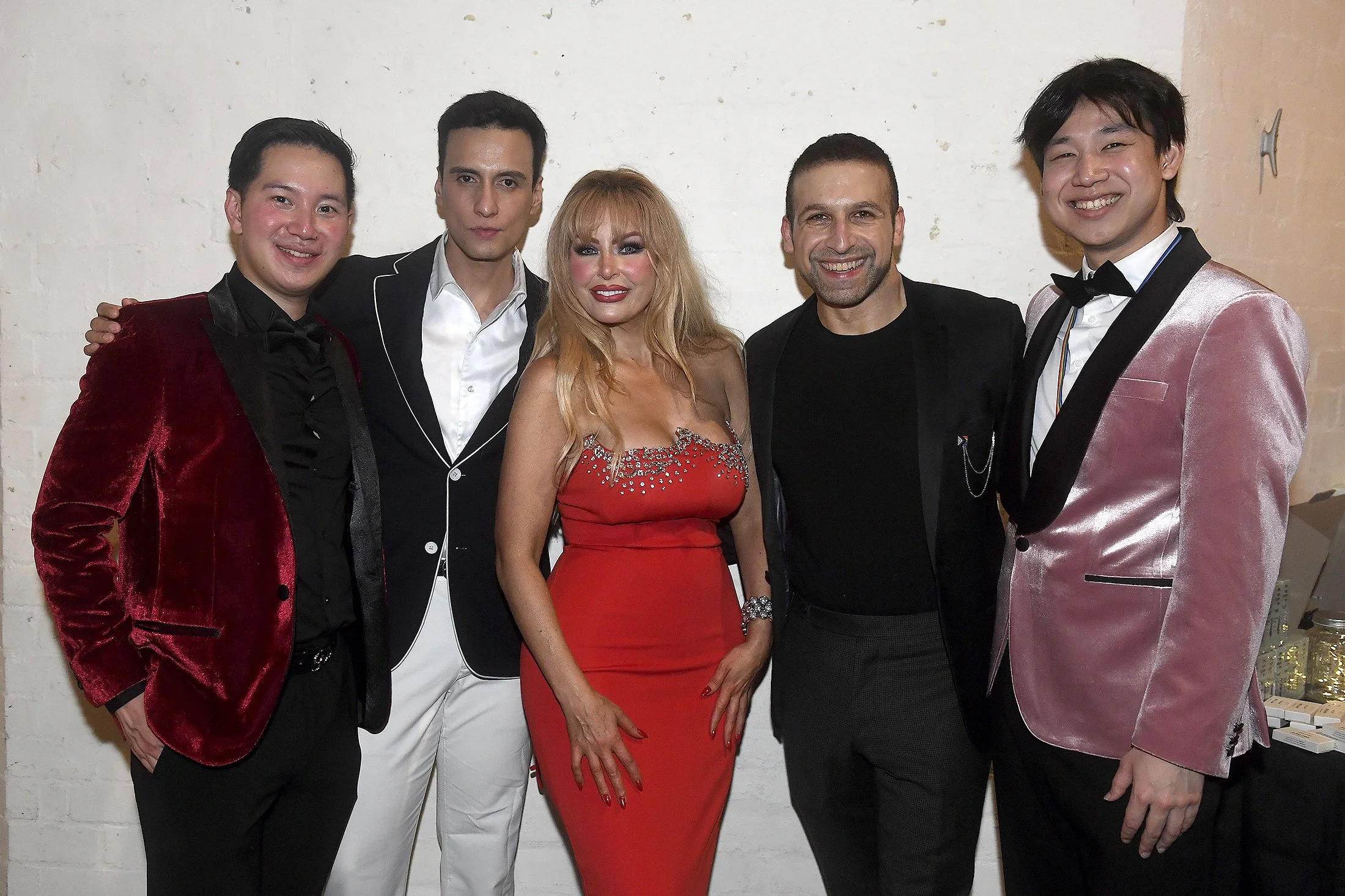 Group of five people dressed in formal attire, posing together in front of a white wall.