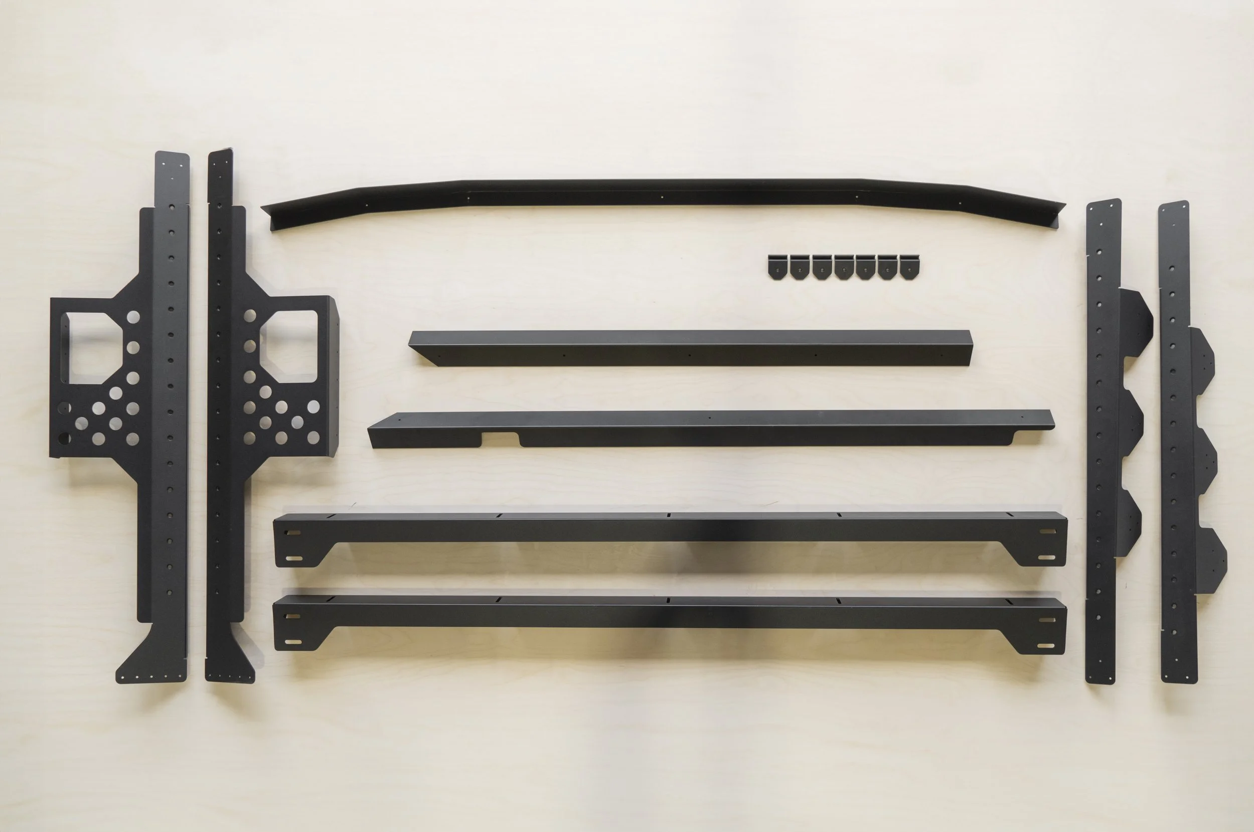 Various black metal parts and brackets laid out on a light surface, likely components for assembling furniture or equipment.