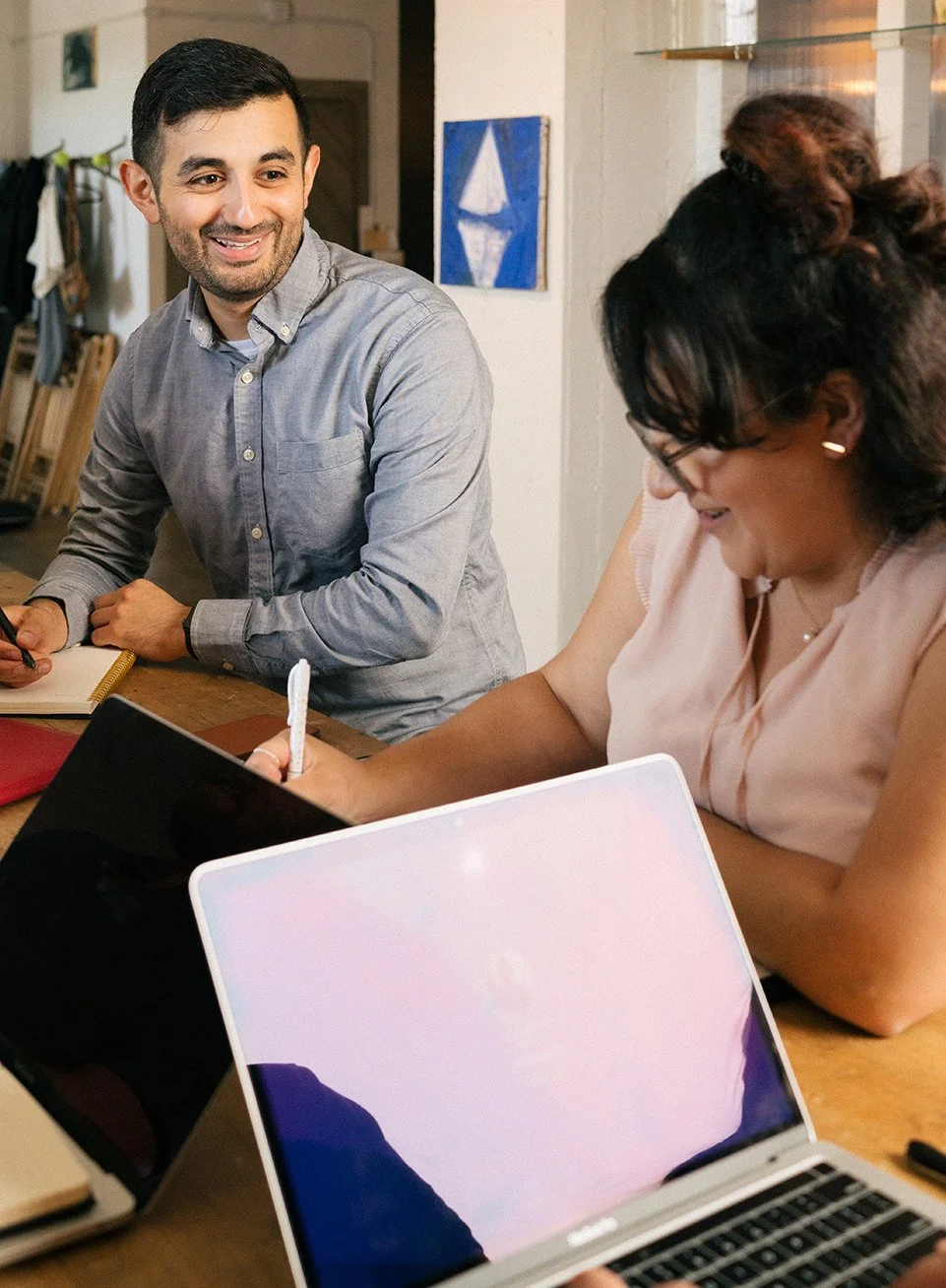 Two employees smiling and taking notes during a team meeting.