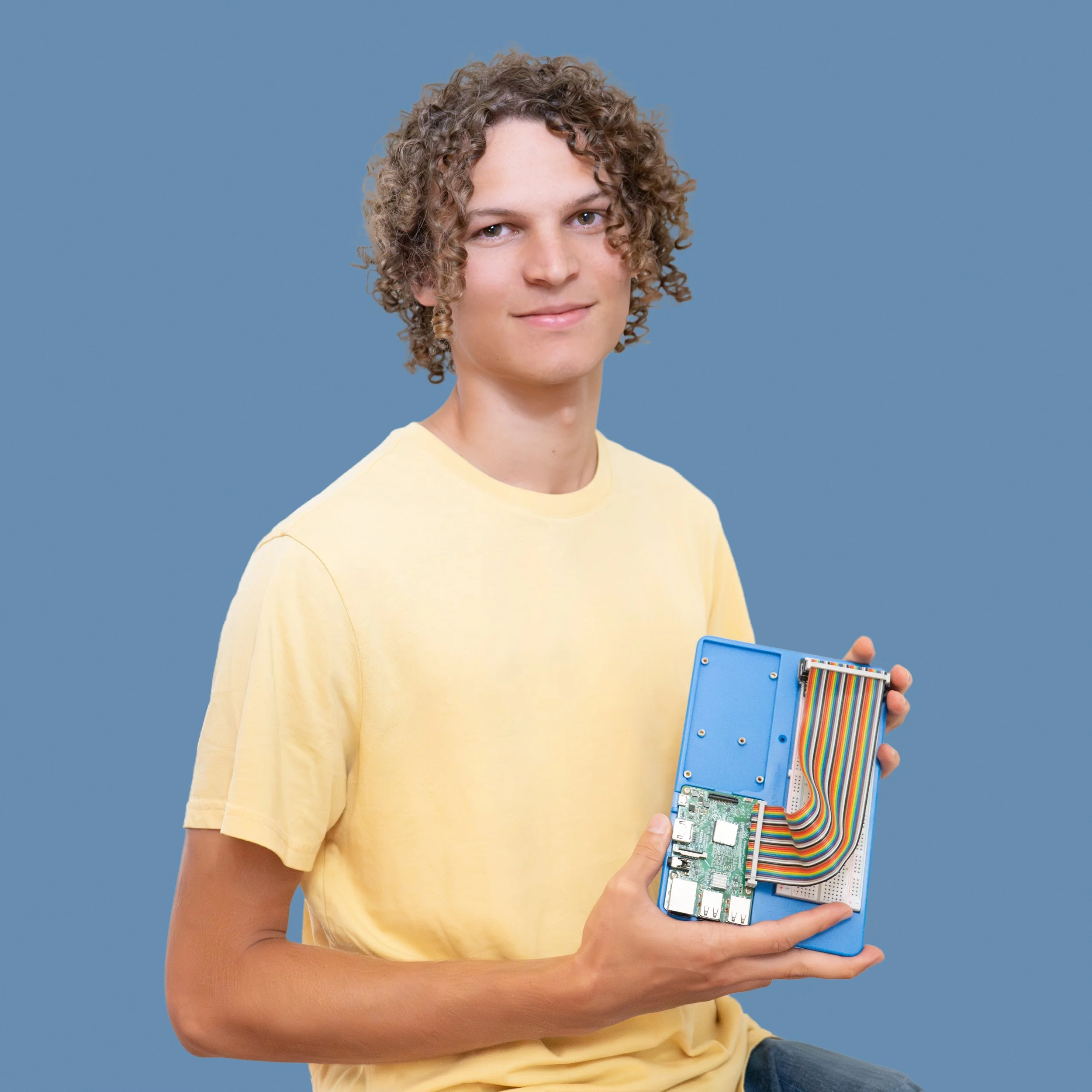 A young man with long brown hair and glasses holds a digital tablet and stylus.