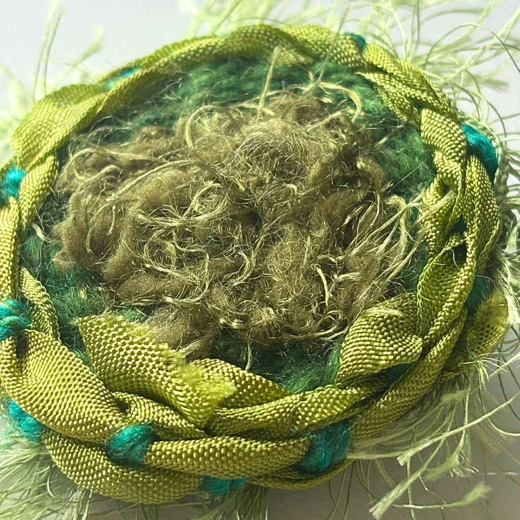 A handwoven brooch woven from textural green yarns and fibres