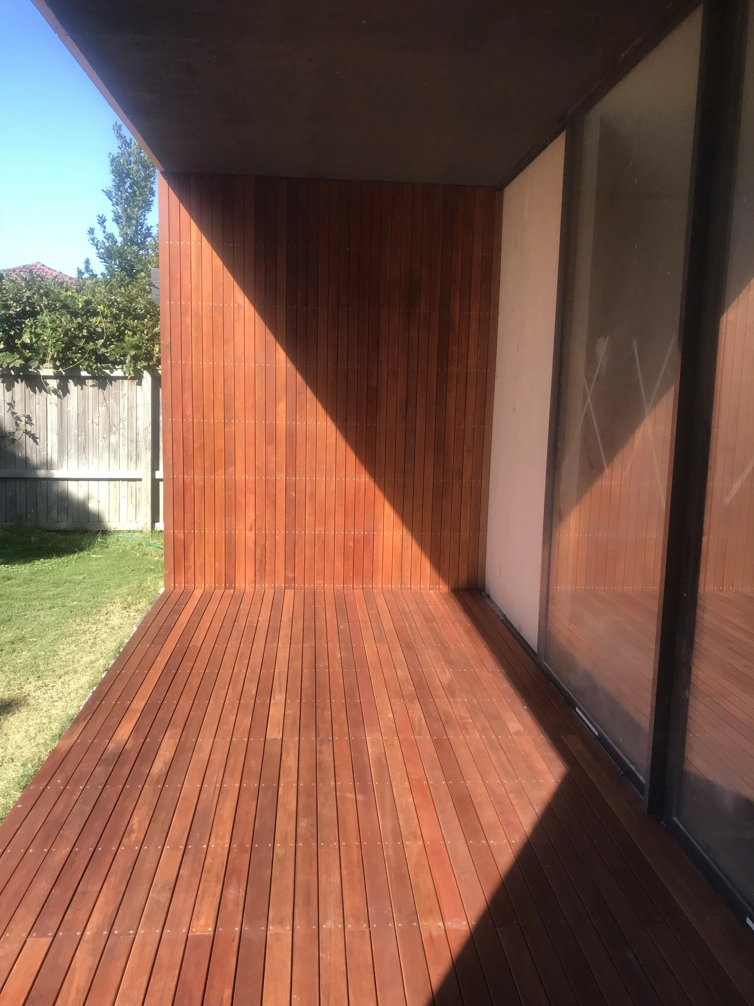 Empty wooden balcony with redwood flooring and wall, glass sliding door on the right.