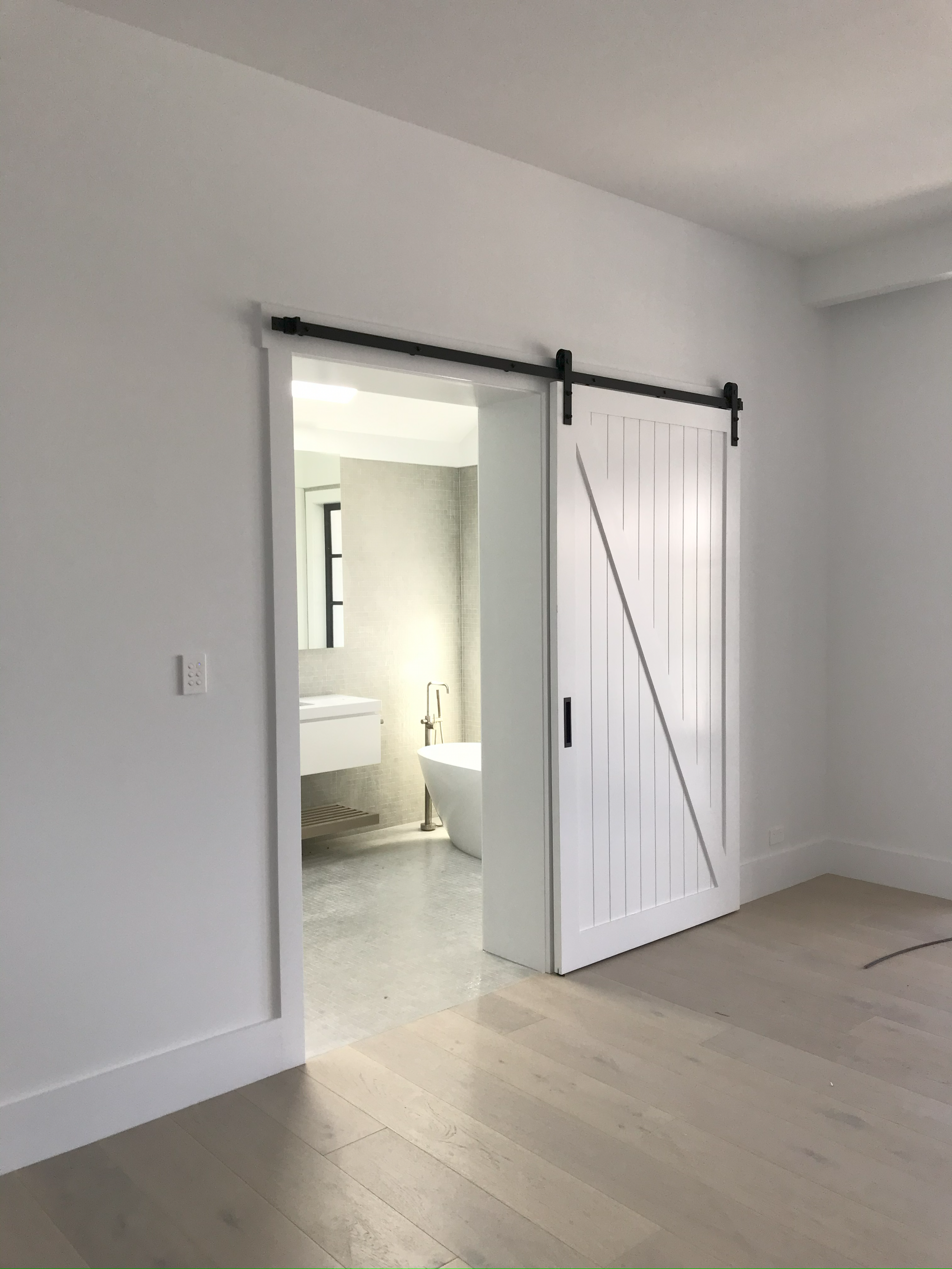 Empty room with a sliding barn door leading to a modern bathroom with a freestanding bathtub and vanity